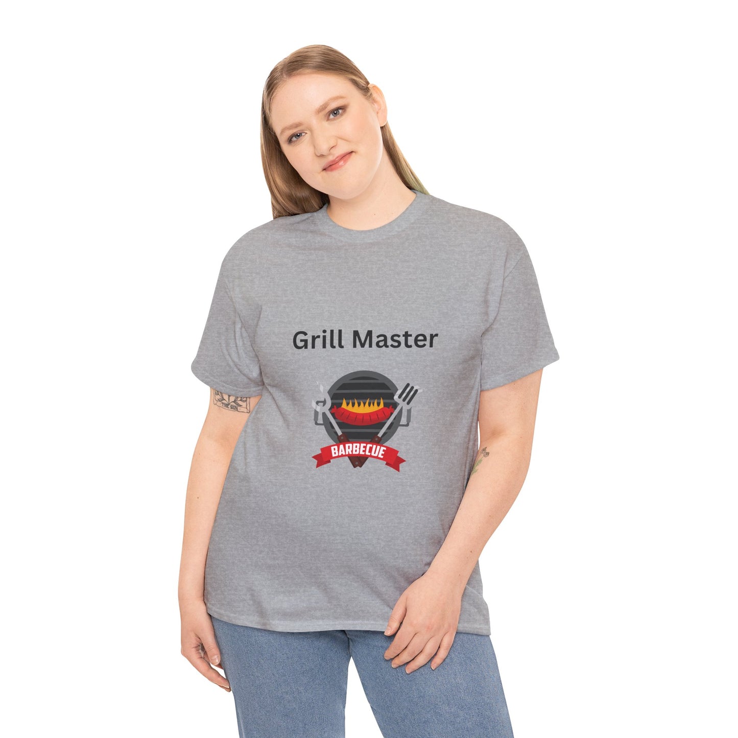 A person wearing a gray Unisex Grill-Master T-shirt: 2 colors; Cotton; Gildan by Printify, proudly made in America, and adorned with a "Grill Master" barbecue graphic and text, stands with a slight smile.