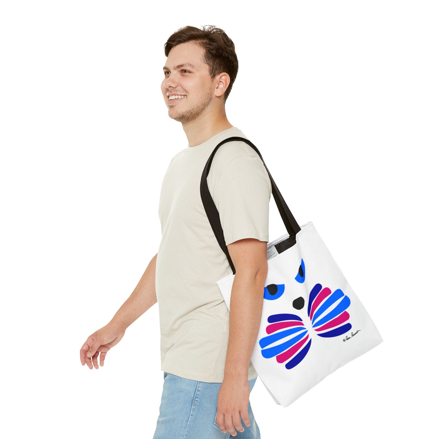 A person in a light shirt and blue jeans is walking and smiling while carrying the Printify Cat-Face Tote Bag. This bag, available in 3 sizes, features a colorful abstract design on durable polyester with a two-sided print, making it perfect for cat lovers who blend style and functionality.