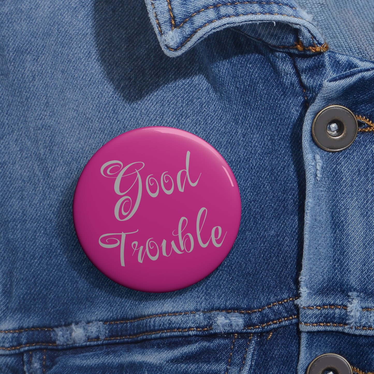 The Good Trouble Pin Button: Political Activism Badge by Printify, featuring white script on pink, is pinned to a blue denim jacket—an eye-catching accessory for enamel pin lovers.