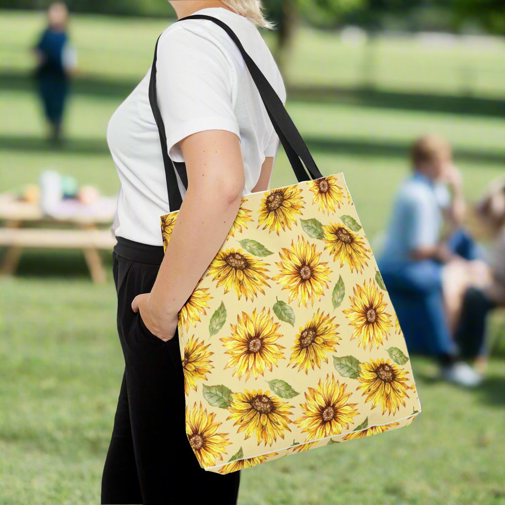 A person wearing a white t-shirt and black pants carries a large Yellow Floral Tote Bag with sunflower print from Printify.