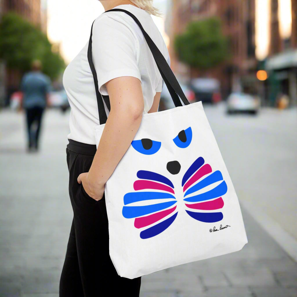 A person stands on a city street with Printify's Cat-Face Tote Bag, made of durable polyester and featuring a vibrant 2-sided print that resembles butterfly wings. Blurred buildings and trees in the background add charm, making it perfect for cat lovers with an eye for style.