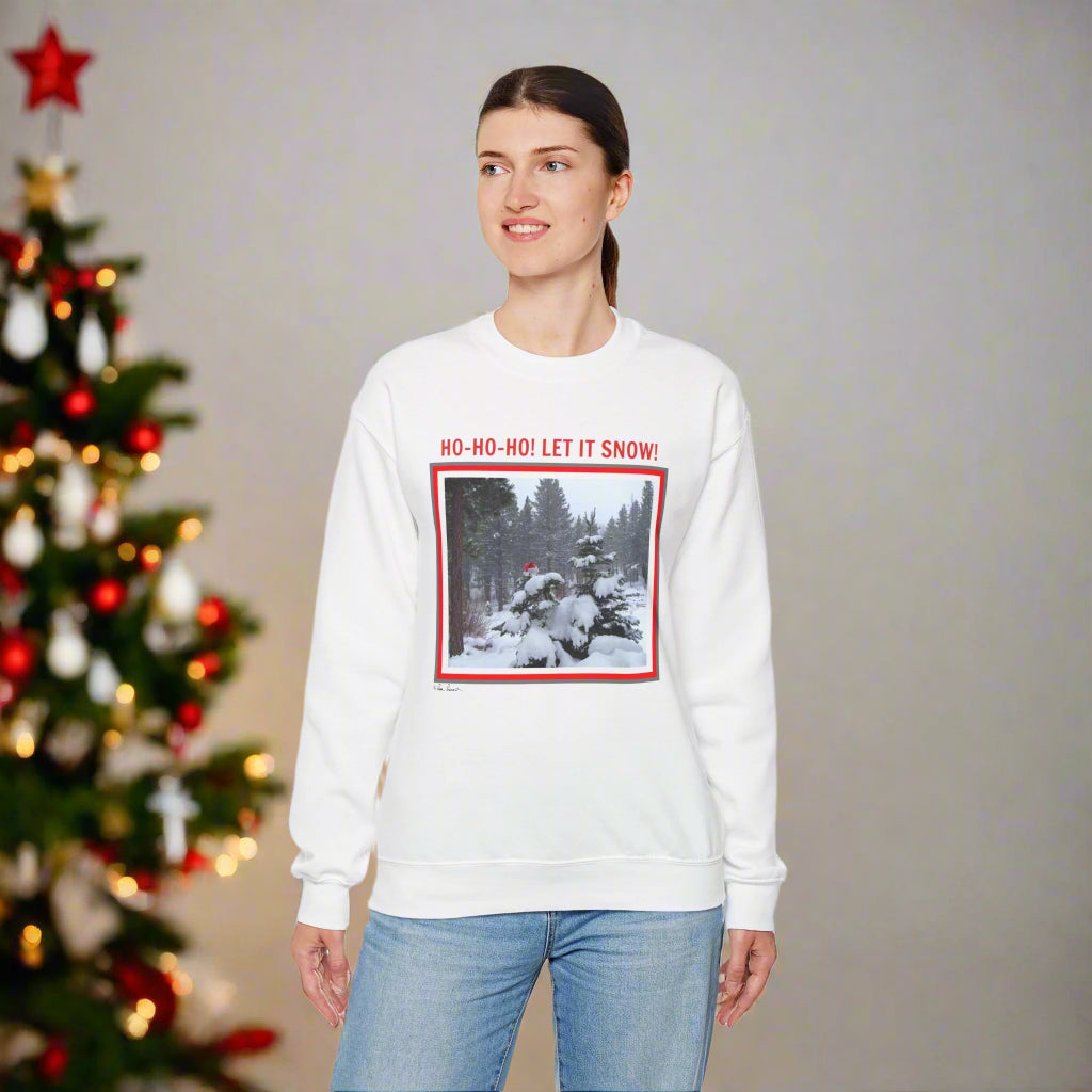 Someone wearing a Printify Unisex Holiday Crewneck Sweatshirt: Heavy Blend™| Santa, with a winter scene and "HO-HO-HO! LET IT SNOW!" design, stands by a decorated Christmas tree.