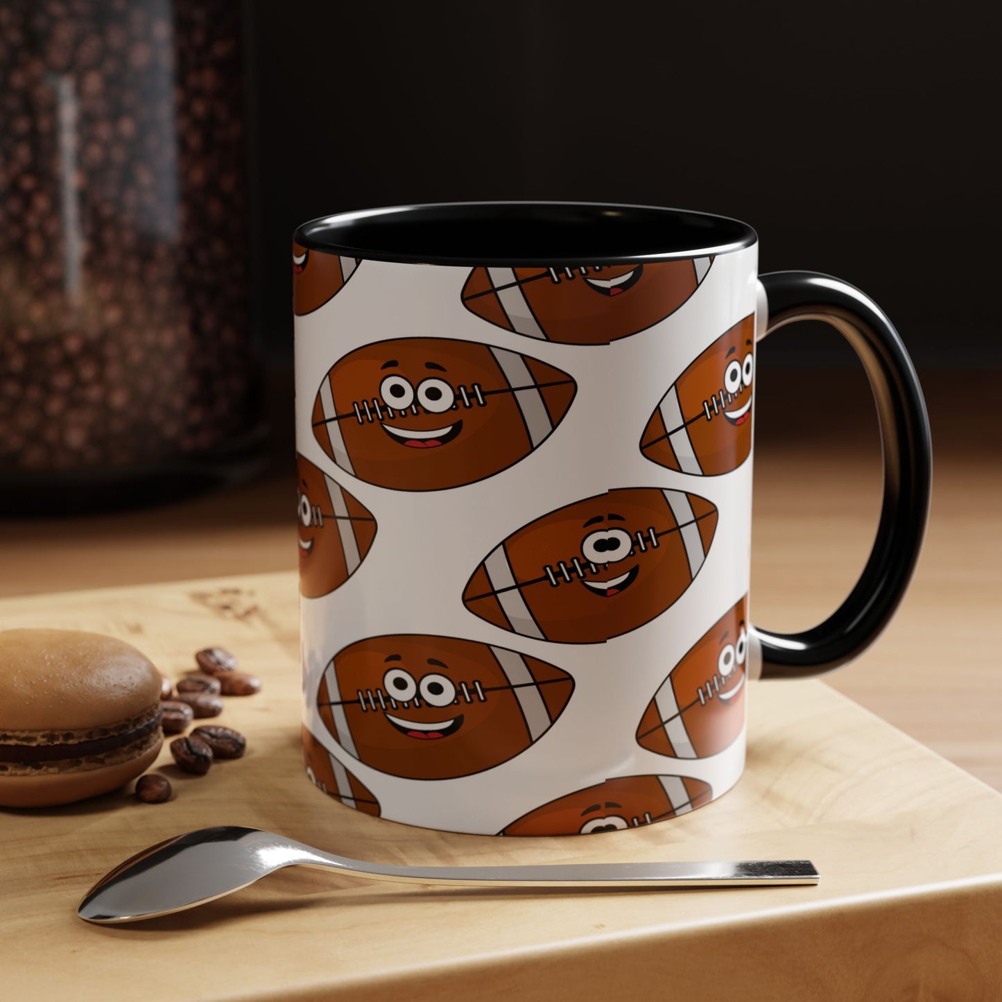 A Printify Happy Football-Faces Mug, 11 oz., BPA-free ceramic with a cartoon design and vibrant colors, is placed on a wooden surface next to a spoon, coffee beans, and a macaron.