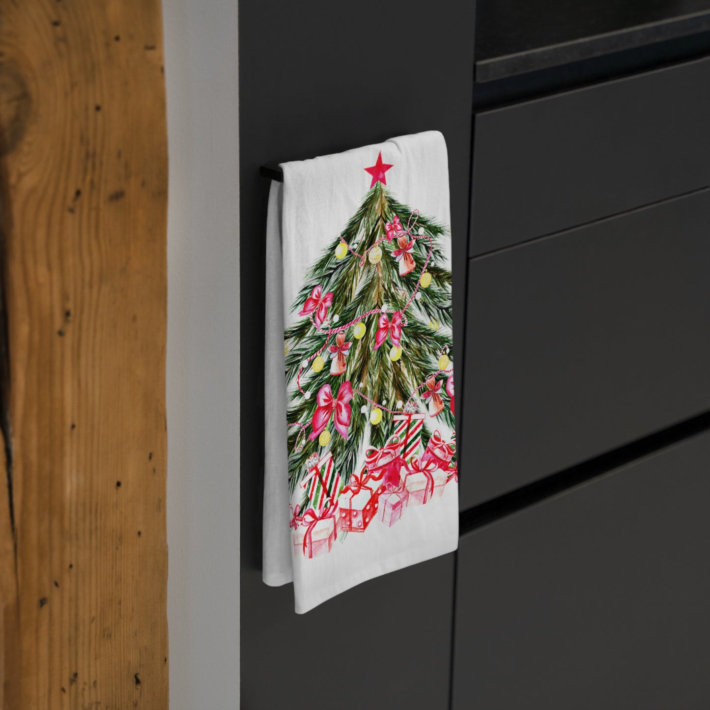 The Large Christmas-Tree Kitchen Towel by Printify, measuring 28" x 28" and made from cotton, adds a festive touch to your kitchen. Hanging on a handle, it showcases a beautifully decorated Christmas tree with wrapped gifts at the base—perfect holiday décor for your home.