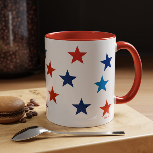A Printify Patriotic Coffee Mug: 11 oz.; 2 Accent colors; Ceramic with red and blue stars, featuring a red interior and handle, sits on a wooden surface beside a silver spoon, a brown macaron, and scattered coffee beans. This American-made mug is also dishwasher and microwave safe.