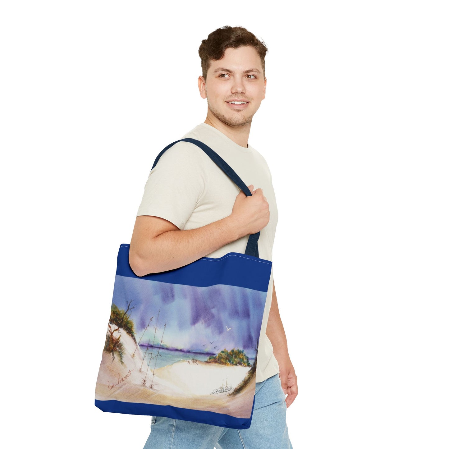 A man in a beige shirt holds a Printify Seaside Tote Bag, featuring a double-sided beach scene on polyester, ideal for summer adventures, against a white background.