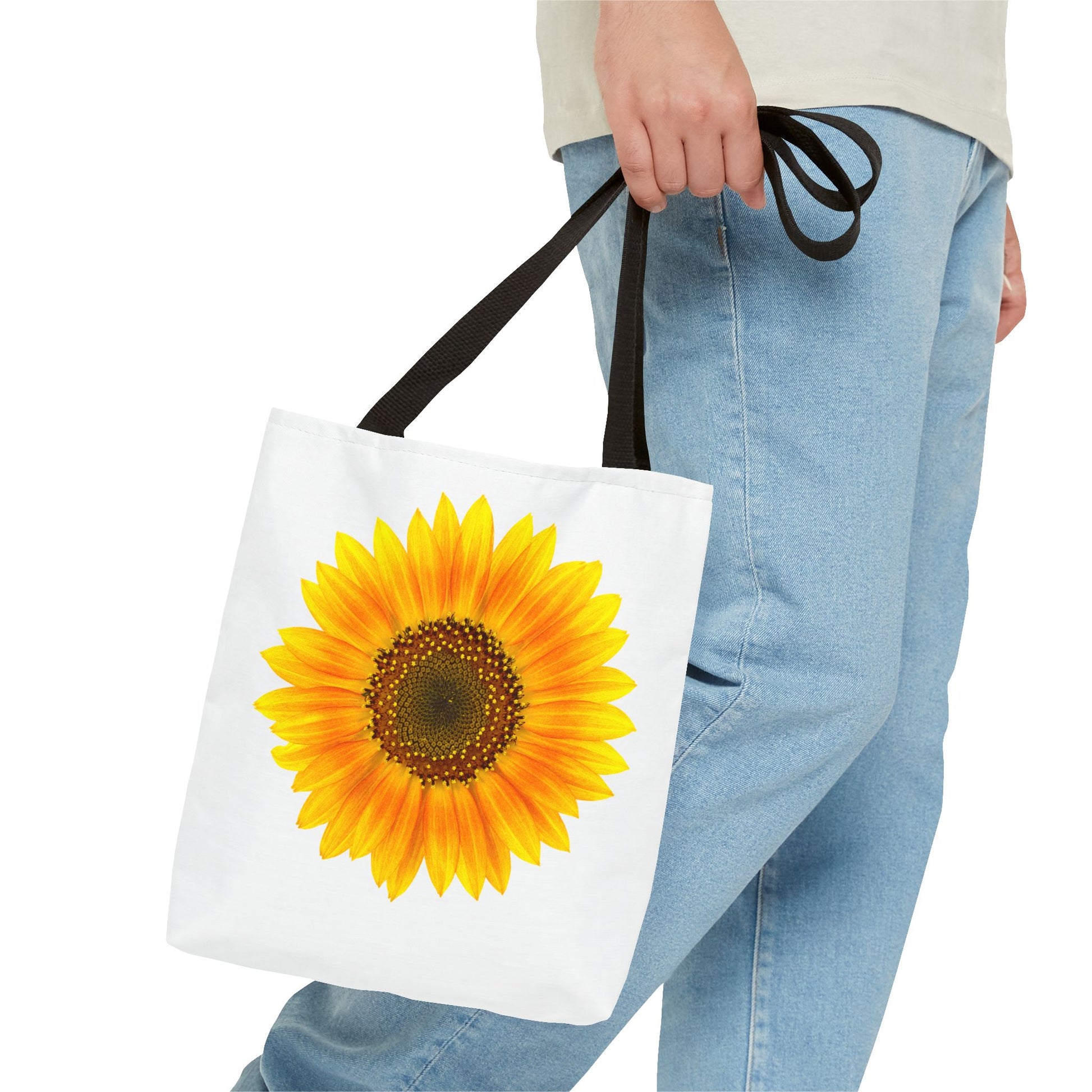 A person carrying a Printify Sunflower Tote Bag in a vibrant, sunny polyester print, wearing light blue jeans and a light-colored shirt.