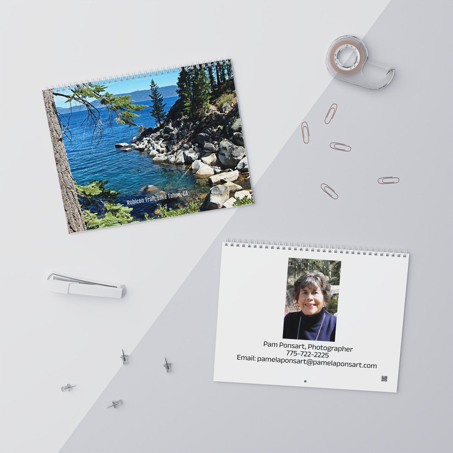 The Printify Minimalist 2025 Wall Calendar: Photographic has a serene beach scene on the cover and contact details for a photographer, creating an inspirational atmosphere. Nearby, office supplies including a stapler, tape, paperclips, and pushpins remain neatly organized.