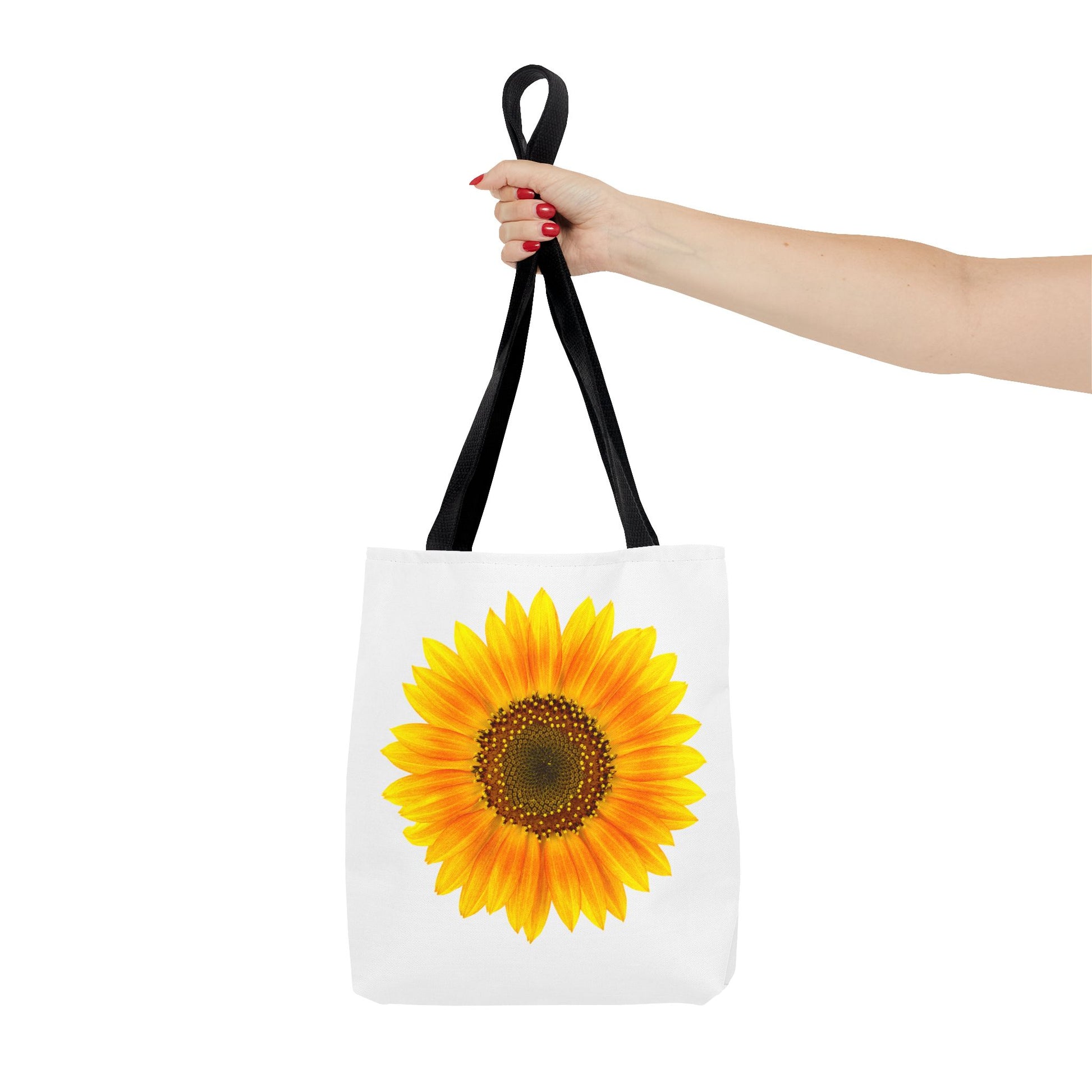 A hand holds a Printify sunflower tote bag, highlighting its nature-inspired design. The 2-sided polyester print features a big sunflower, adding a vibrant, sunny touch against the plain background. Available in 3 sizes with black handles.