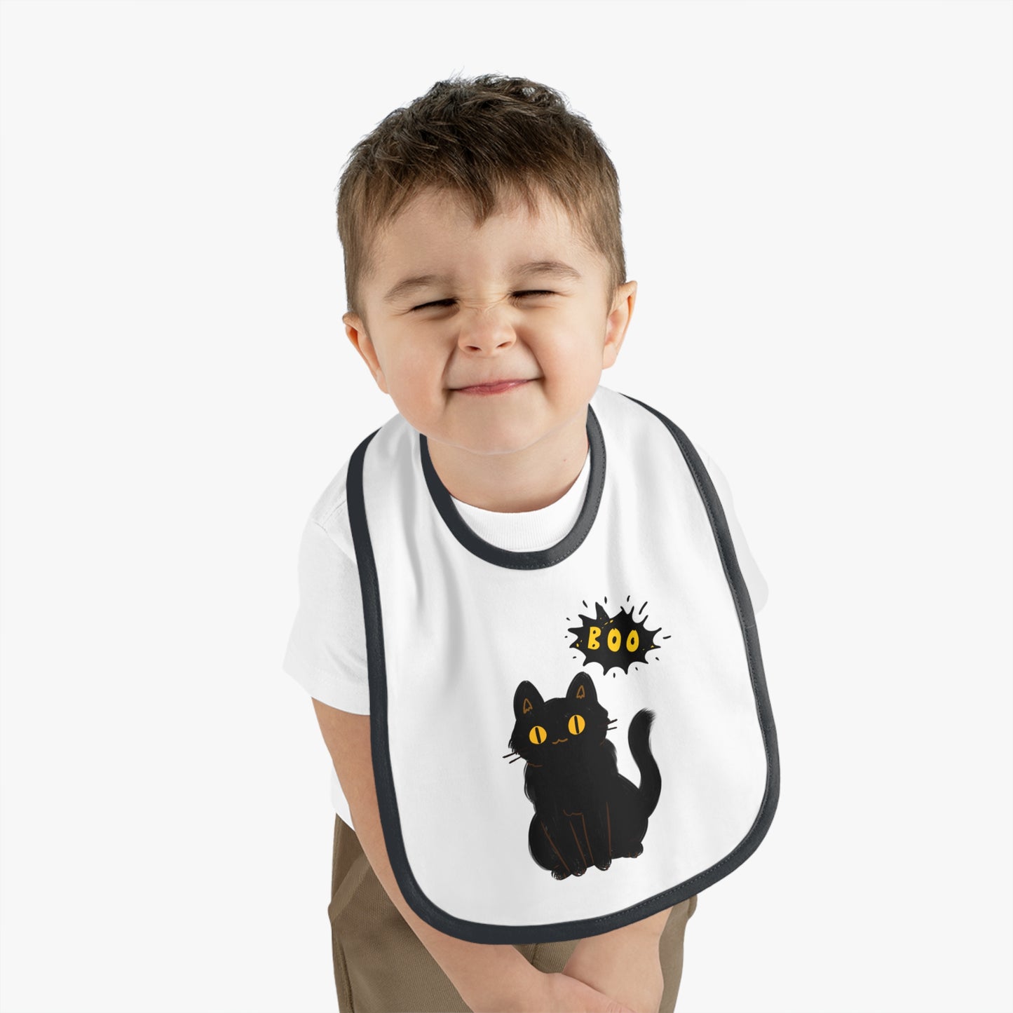 A young child smiles with eyes closed, wearing the Printify Halloween Cat Baby Bib: Cotton | Spooky Cute | Babyware—featuring a black cat and “Boo”—the perfect Halloween gift for babies.