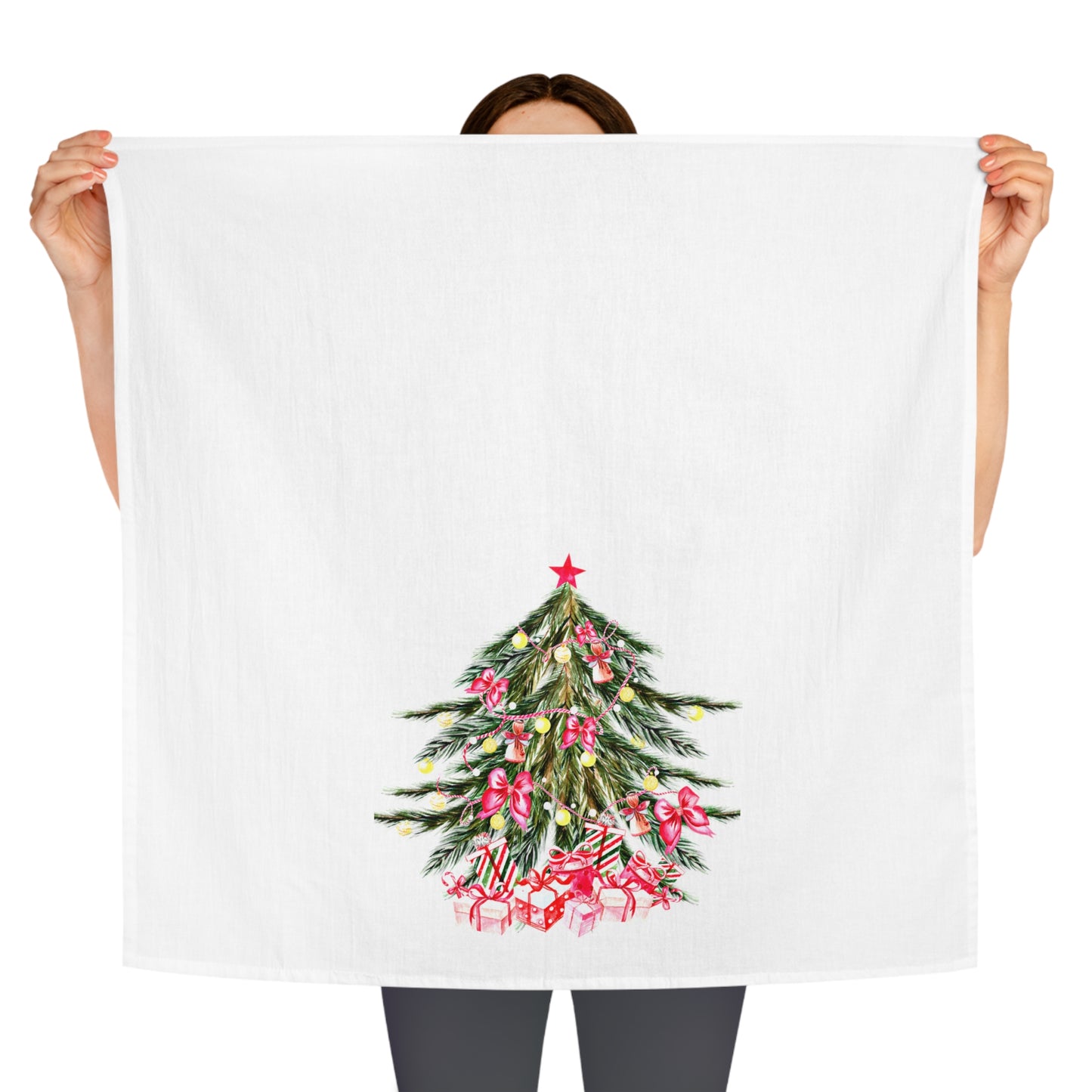 A person holding up a Printify Christmas-Tree Kitchen Towel, featuring a vibrant tree and red gifts, adds a festive touch to your holiday décor. This large cotton towel measures 28" x 28".