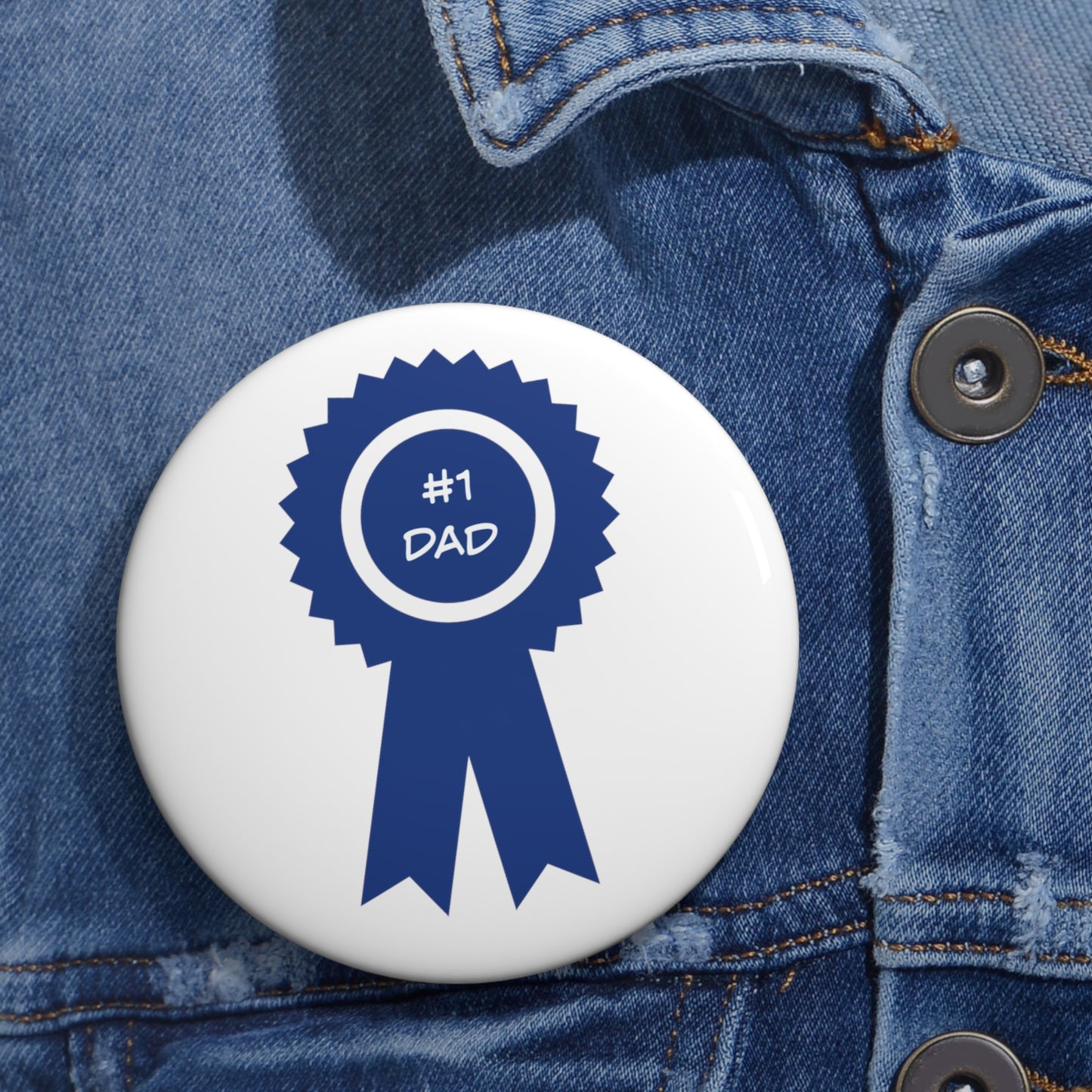 A Printify #1 Dad Button: 2 sizes; Lightweight metal; Graphics is pinned with a safety pin on a blue denim jacket.