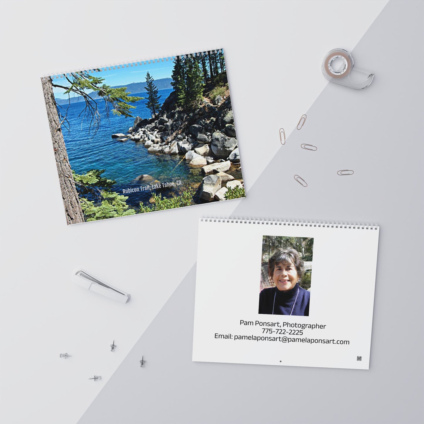 Overhead view of two calendars: a Printify Minimalist 2025 Wall Calendar showcasing a lakeside scene and another 2025 wall calendar featuring Pam Ponsart's portrait with contact info. Surrounded by office supplies, the setup fosters inspiration.