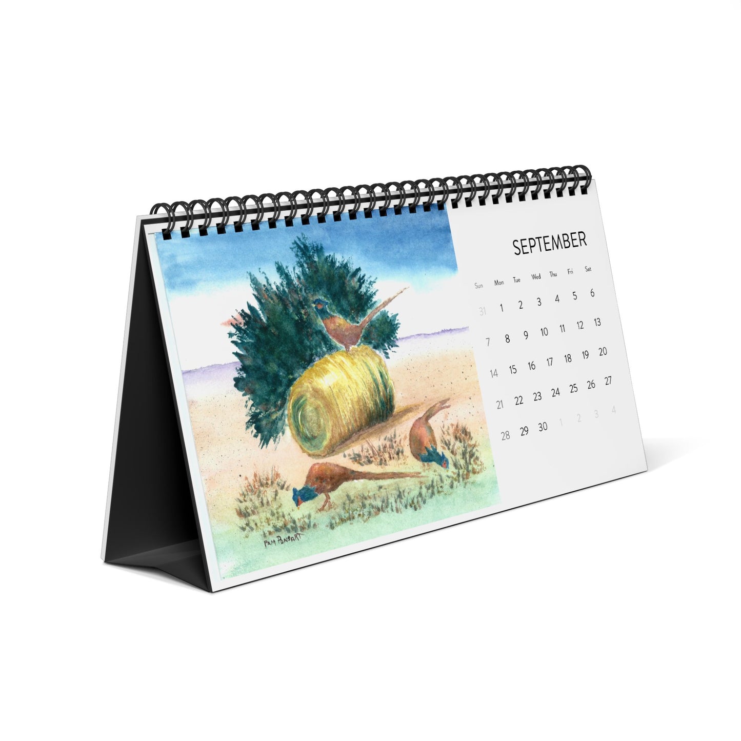 The 2025 Desktop Calendar from Printify, featuring assorted watercolor reproductions, is open to September with an illustration of birds fluttering around a hay bale and bushes in a serene field, echoing the essence of early autumn reminiscent of Pam Ponsart's art.