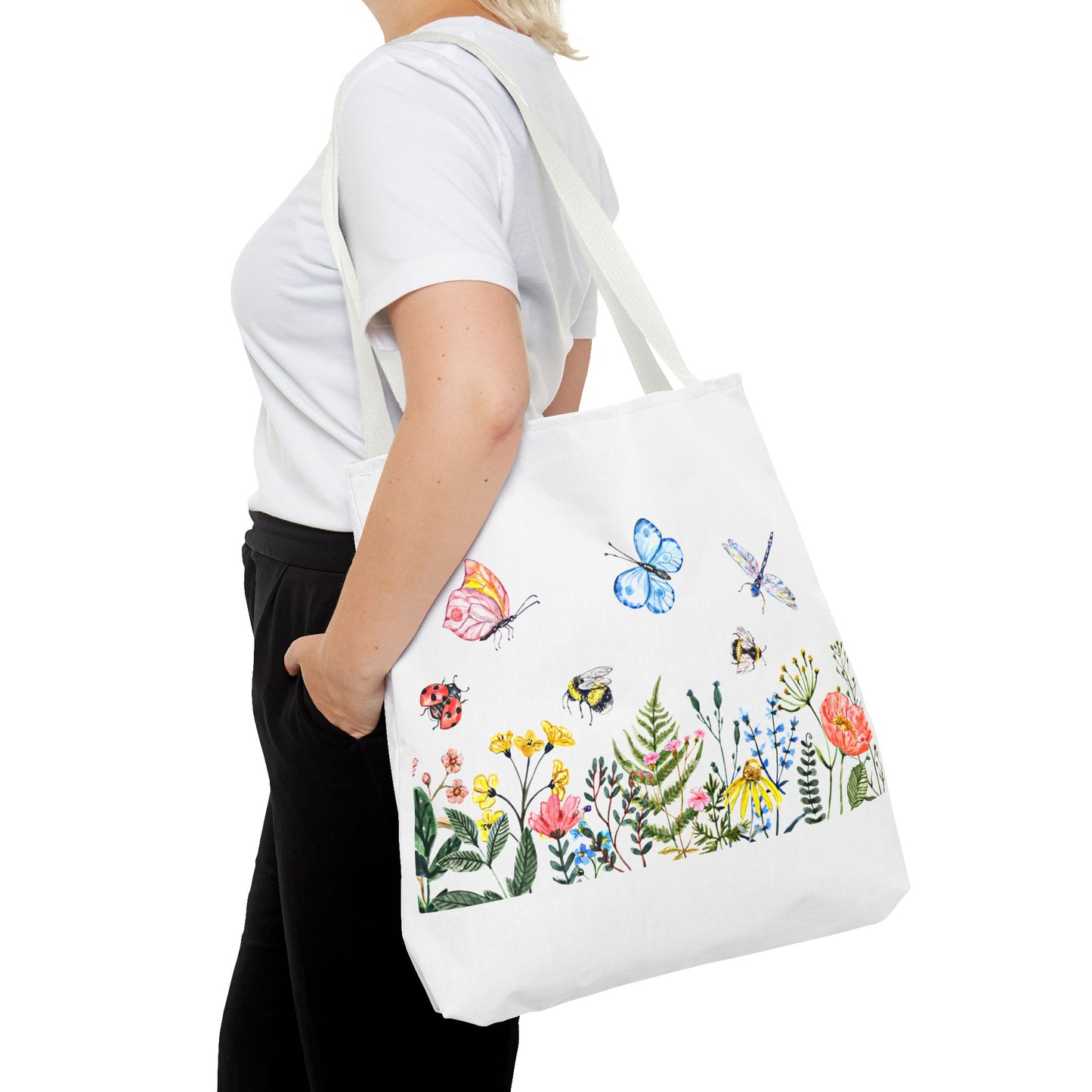 A person holds a Printify Spring Garden Tote Bag, displaying vibrant 2-sided polyester prints of colorful insects and flowers, available in 3 sizes.