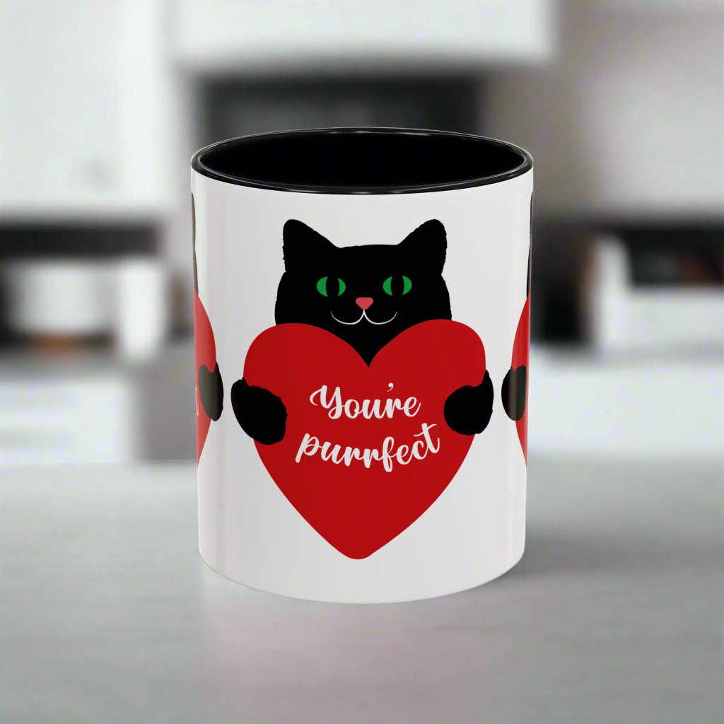 The Purrfect Love Cat-Mug by Printify, available in 2 colors and sizes, is a ceramic mug featuring a black cat with a red heart and the phrase "You're purrfect." It's the ideal gift for cat lovers to warm hearts and brighten any day.