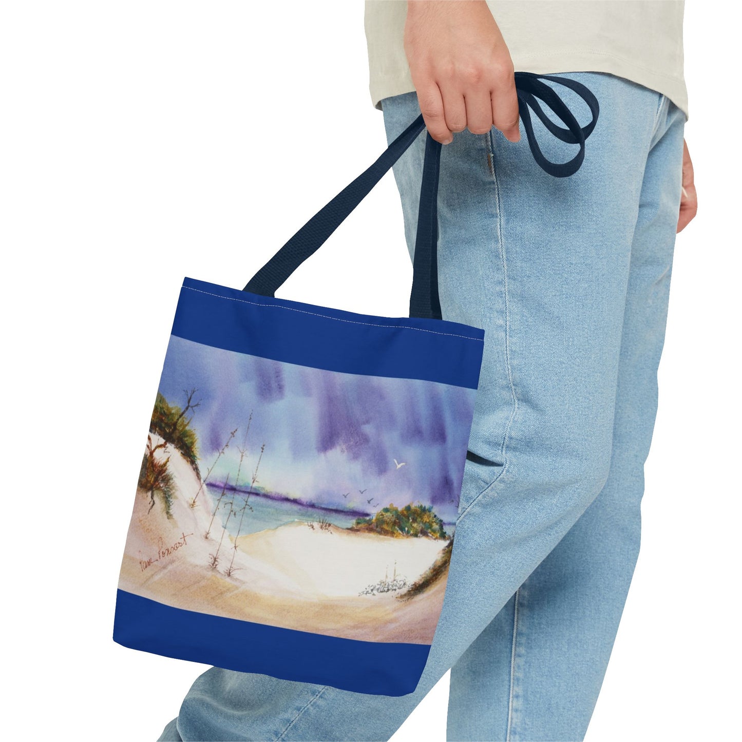 A person is holding a Printify Seaside Tote Bag, available in 3 sizes with a beach painting design on polyester and a 2-sided print, perfect for summer adventures, while wearing light blue jeans and a light-colored shirt.
