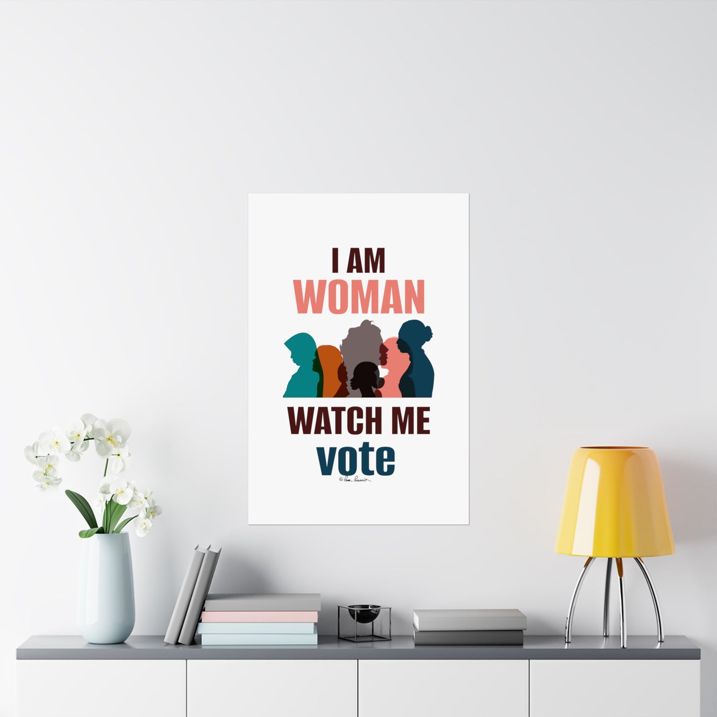 A minimalist room with a floral vase, books, a small container, and a yellow lamp on a white shelf. A poster on the wall, "Voting Womens Posters: 3 sizes; Vertical; Matte finish" from Printify, printed on museum-grade paper using archival inks, reads "I AM WOMAN WATCH ME vote" above silhouettes of women.