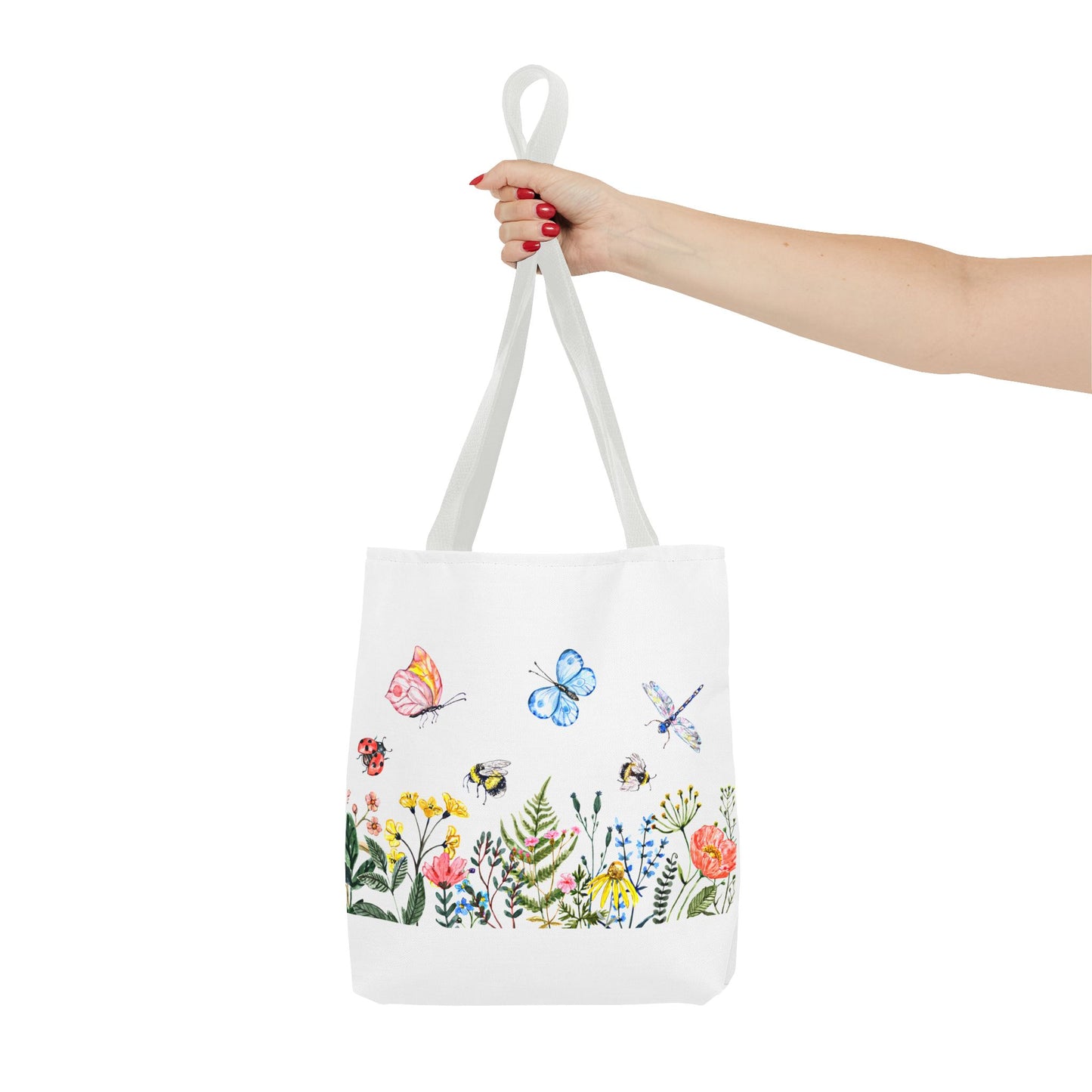 A hand holds the Spring Garden Tote Bag by Printify, a white polyester bag available in 3 sizes, featuring a vibrant 2-sided print with illustrations of butterflies, bees, dragonflies, and wildflowers—ideal for outdoor activities.