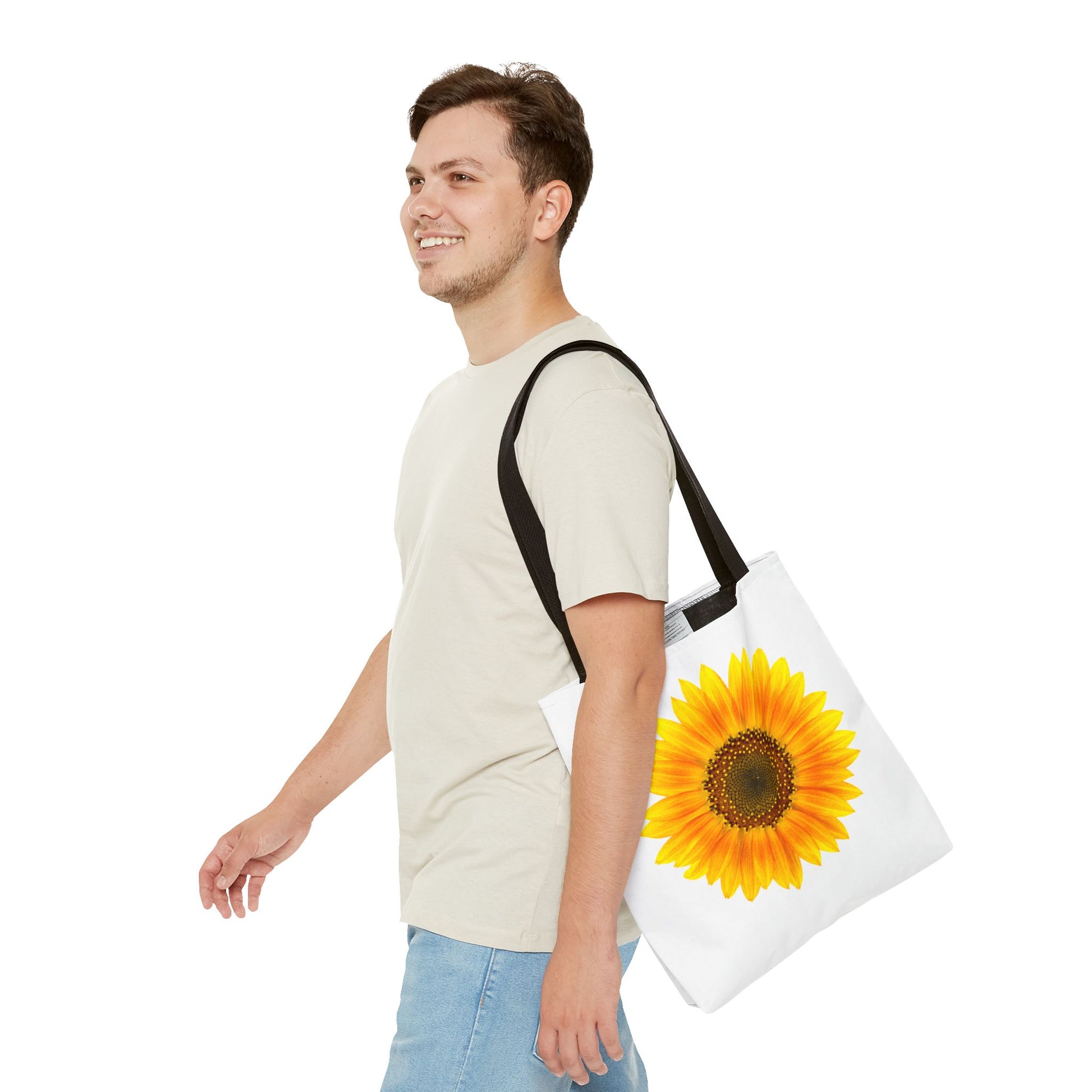 A person in a beige shirt and blue jeans carries a Printify Sunflower Tote Bag, detailed with nature-inspired designs on polyester, smiling as they walk. The tote's vibrant 2-sided print in three available sizes exudes a sunny vibe.