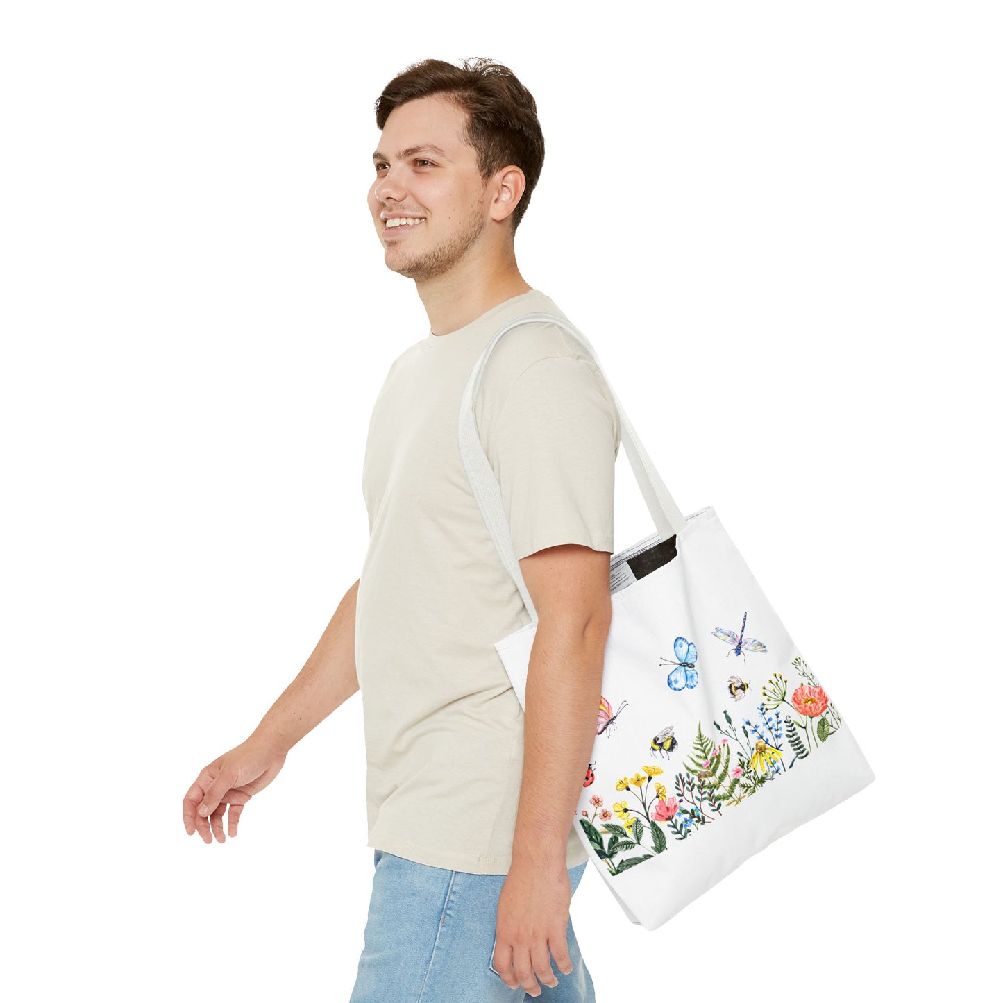 Someone in a light t-shirt and jeans carries a vibrant Printify Spring Garden Tote Bag, featuring colorful floral and insect designs. They walk with a smile, clearly geared up for outdoor fun.