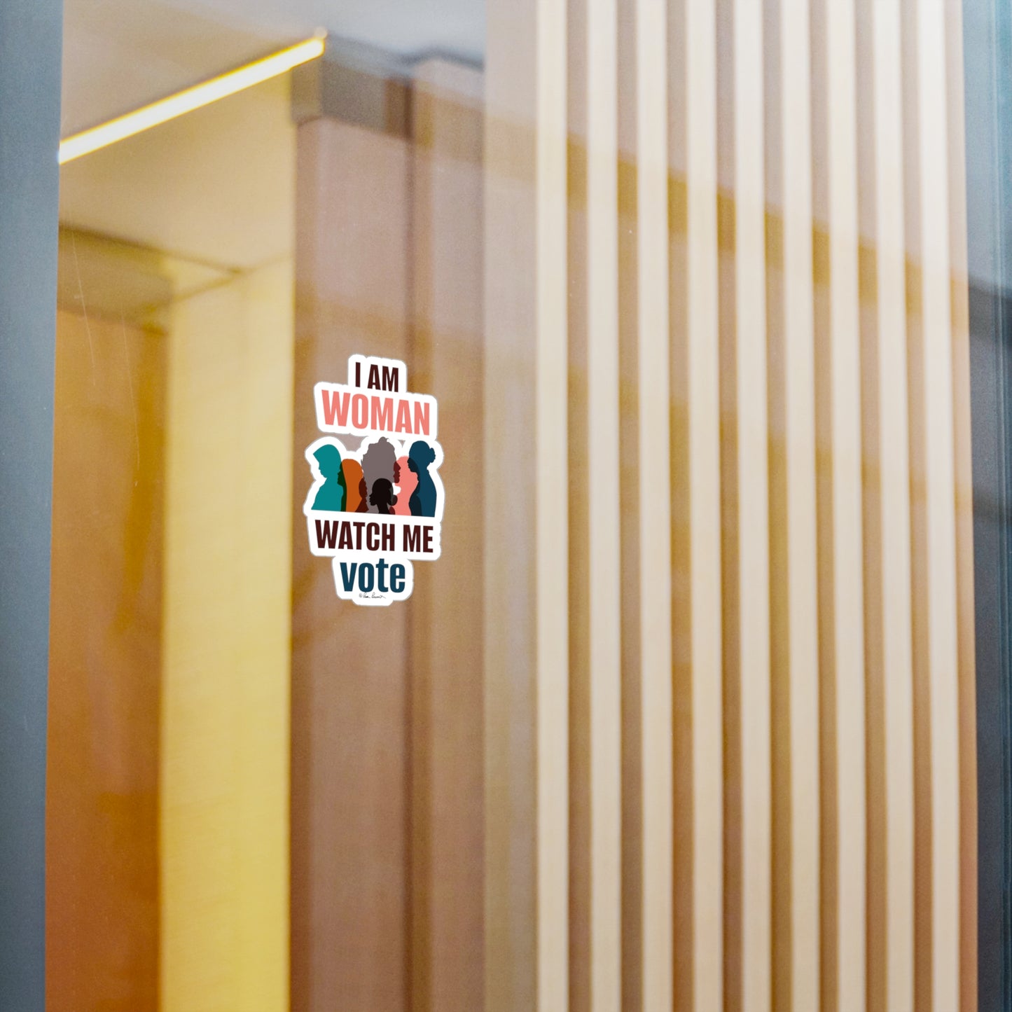Sticker on a glass door reading "i am woman watch me vote" with silhouettes of three women, set against a background of vertical blinds. The Printify Voting Women's Decals features removable adhesive and is made of white vinyl. Available in unisex and 4 sizes with graphics printed on it.