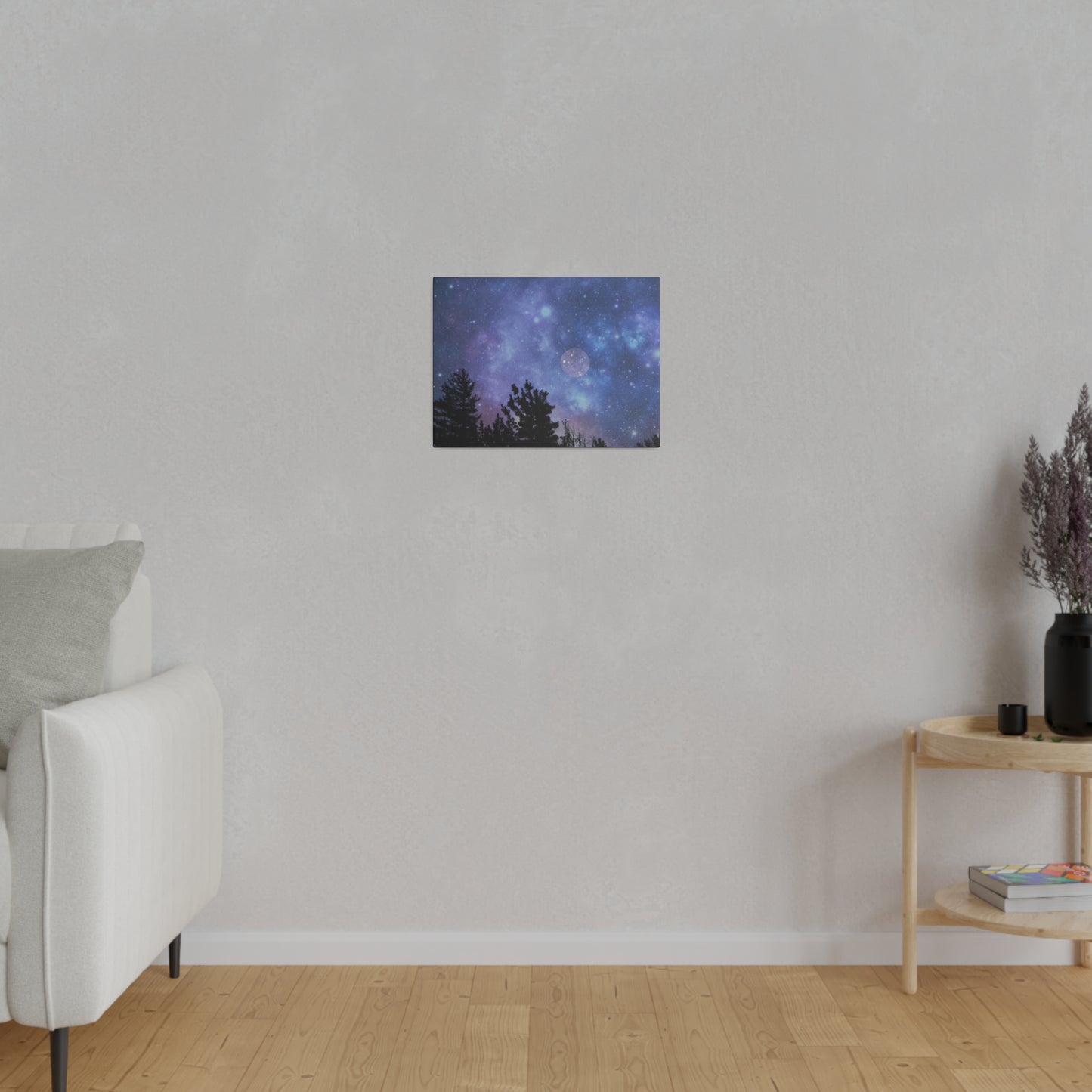A Printify Blue-Moon Matte Canvas depicting a starry night sky, encased in a radial pine frame sourced from renewable forests, hangs on a plain wall in a room with a sofa and a wooden side table.