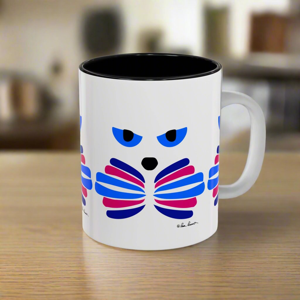 The Cat-Face Coffee Mug by Printify, available in two sizes and crafted from ceramic, showcases a stylized, colorful cat-face design with blue eyes and layered pink and blue elements resembling ribs. It's perfectly placed on a wooden surface, making it an ideal gift for cat lovers who enjoy a touch of Catitude with their morning coffee.