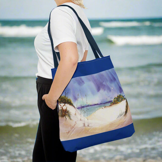 A person stands against a plain background, holding their Printify Seaside Tote Bag with a vibrant beach scene—a perfect summer adventure companion. This polyester bag is available in 3 sizes and features a 2-sided print.