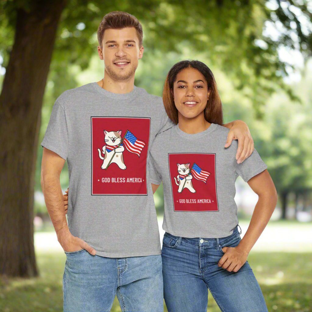 Two people stand outdoors wearing Printify's Unisex Patriotic Cat T-shirts in heavy cotton, featuring a cartoon cat holding an American flag and the text "God Bless America." They have their arms around each other's shoulders.