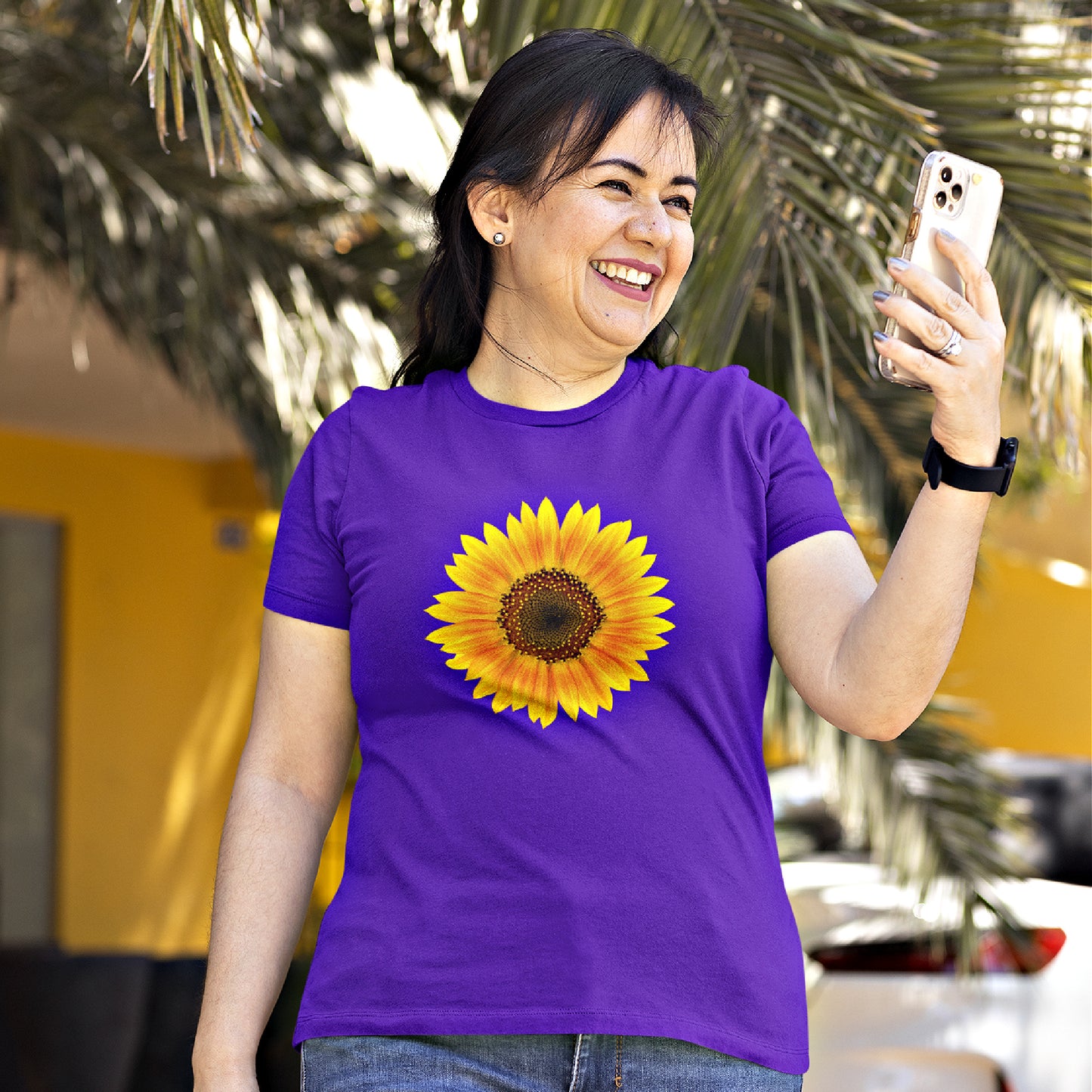 Mock up of a happy woman checking her phone while wearing our purple relaxed-fit t-shirt with sunflower design