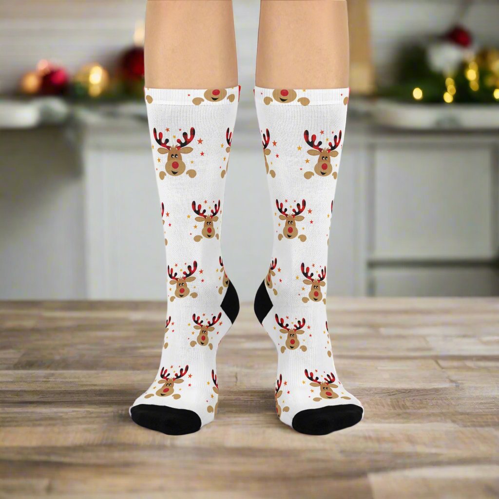 A person stands on a wooden floor wearing Festive Reindeer Crew-Socks from Printify, featuring a unisex design with cheerful reindeer patterns and cushioned bottoms for added comfort.