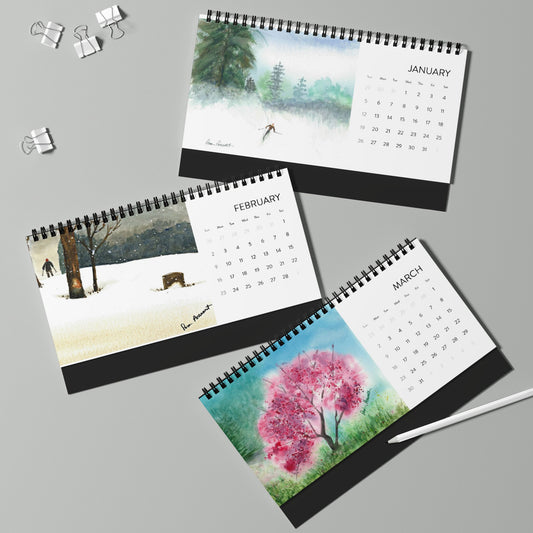 Three pages from the 2025 Desktop Calendar: Assorted Watercolor reproductions by Printify are elegantly displayed on a table with a pen and binder clips, each presenting stunning seasonal artwork in delicate watercolor style.