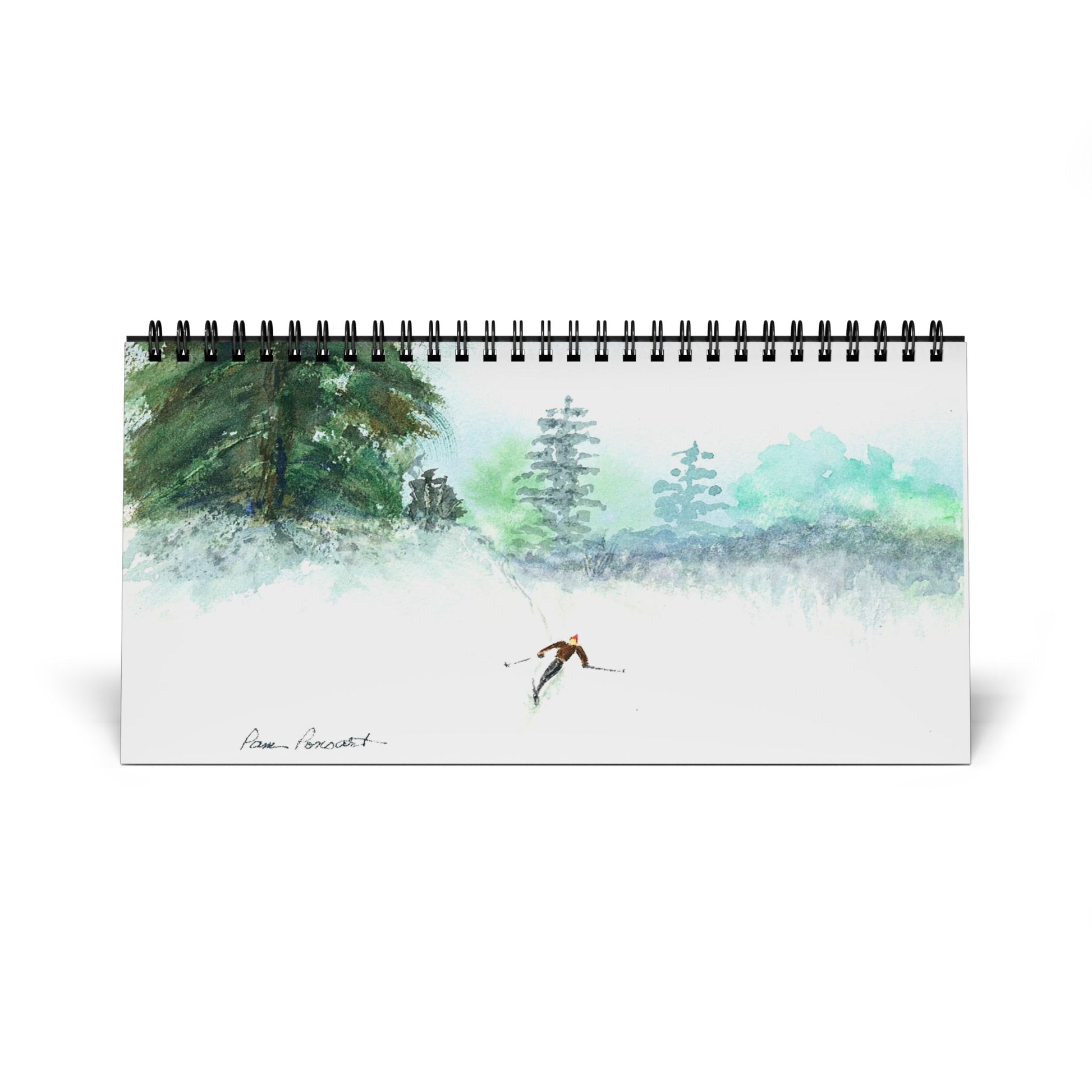 The 2025 Desktop Calendar by Printify features vibrant watercolor reproductions, including a Pam Ponsart painting of a skier in a snowy, tree-lined landscape.