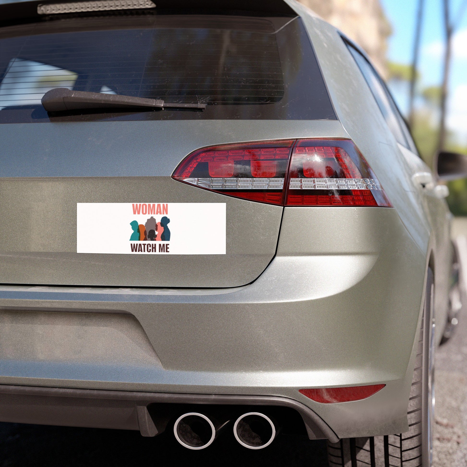 A gray hatchback car showcasing a weatherproof vinyl car magnet from Printify, featuring colorful silhouettes of women and the slogan "WOMAN WATCH ME," prominently displayed on the rear.