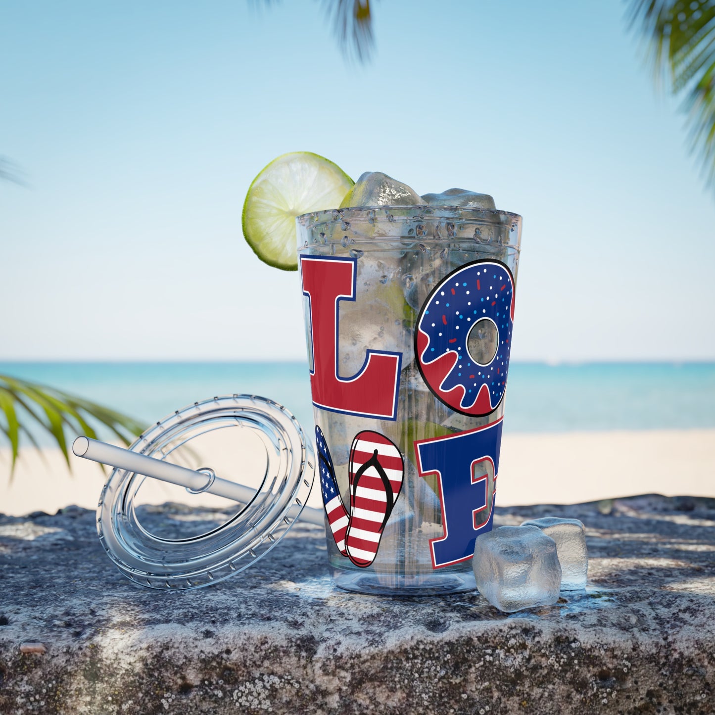 A Love USA tumbler by Printify with a lime and a straw sitting on the beach.