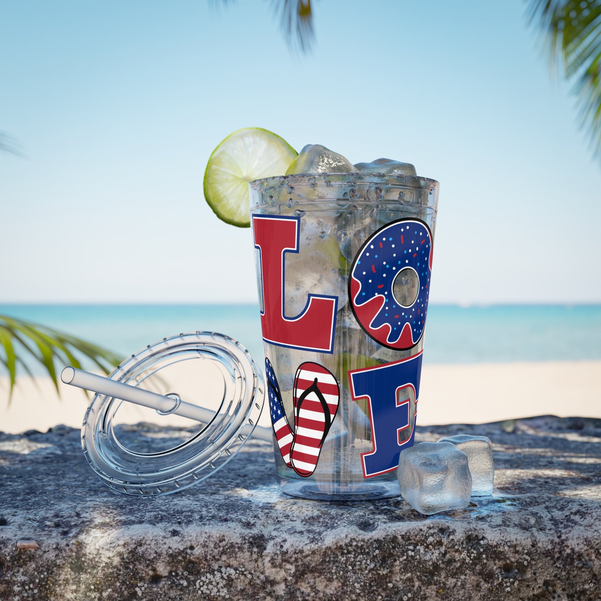 A Love USA tumbler by Printify with a lime and a straw sitting on the beach.