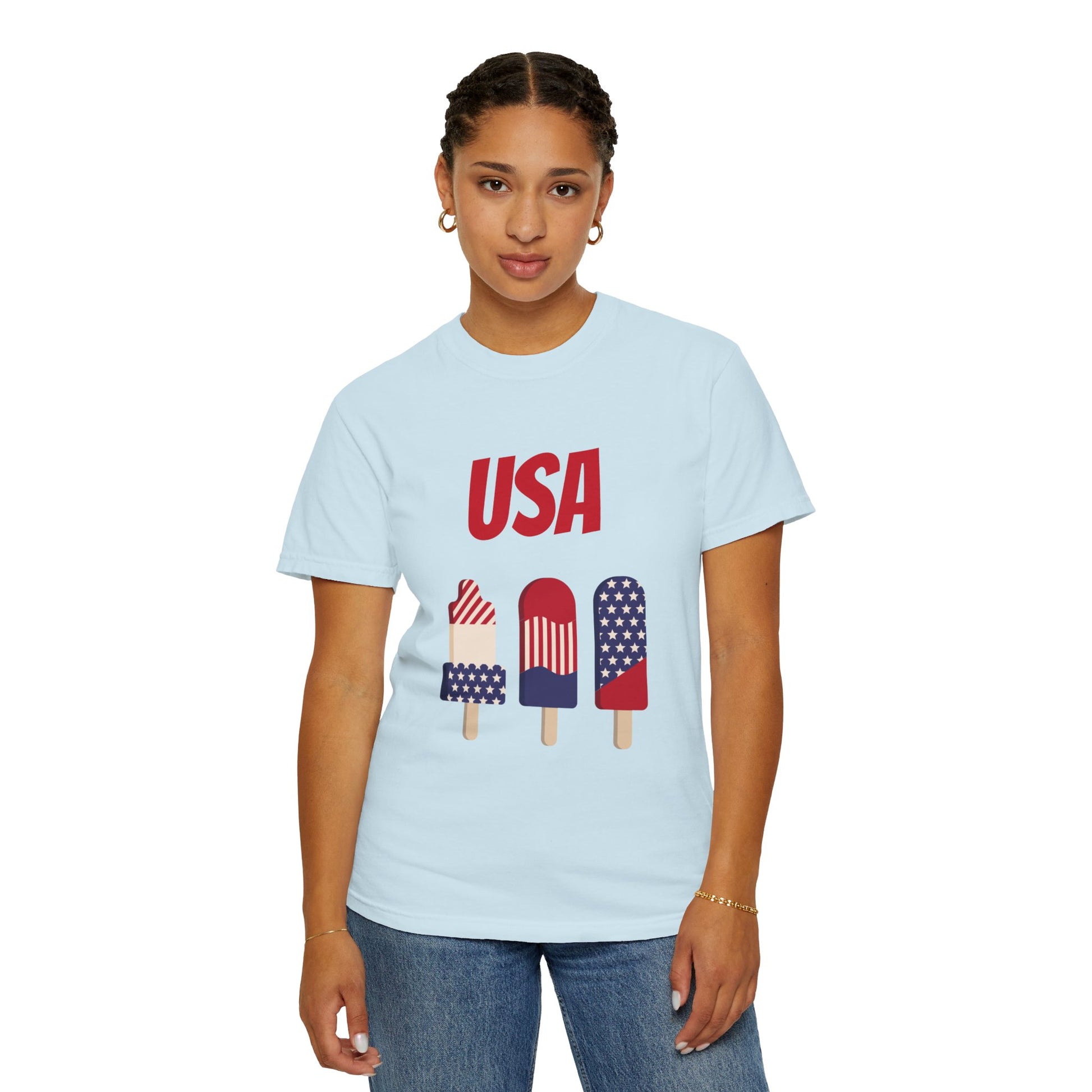 Person wearing a light blue Unisex USA T-shirt: 3 colors; Cotton; Comfort Colors 1717 by Printify, made of 100% ring-spun cotton, with "USA" printed above three popsicles decorated in American flag patterns, standing against a plain background.