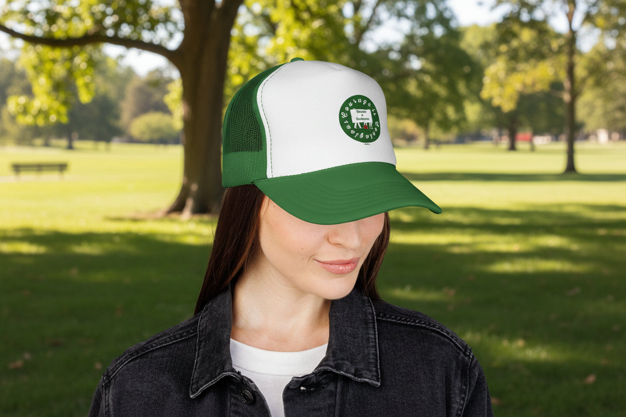 A person wearing the green and white Printify Vintage Trucker Hat: Courage is Contagious Logo Mesh Cap stands outdoors in a park with trees and grass in the background.