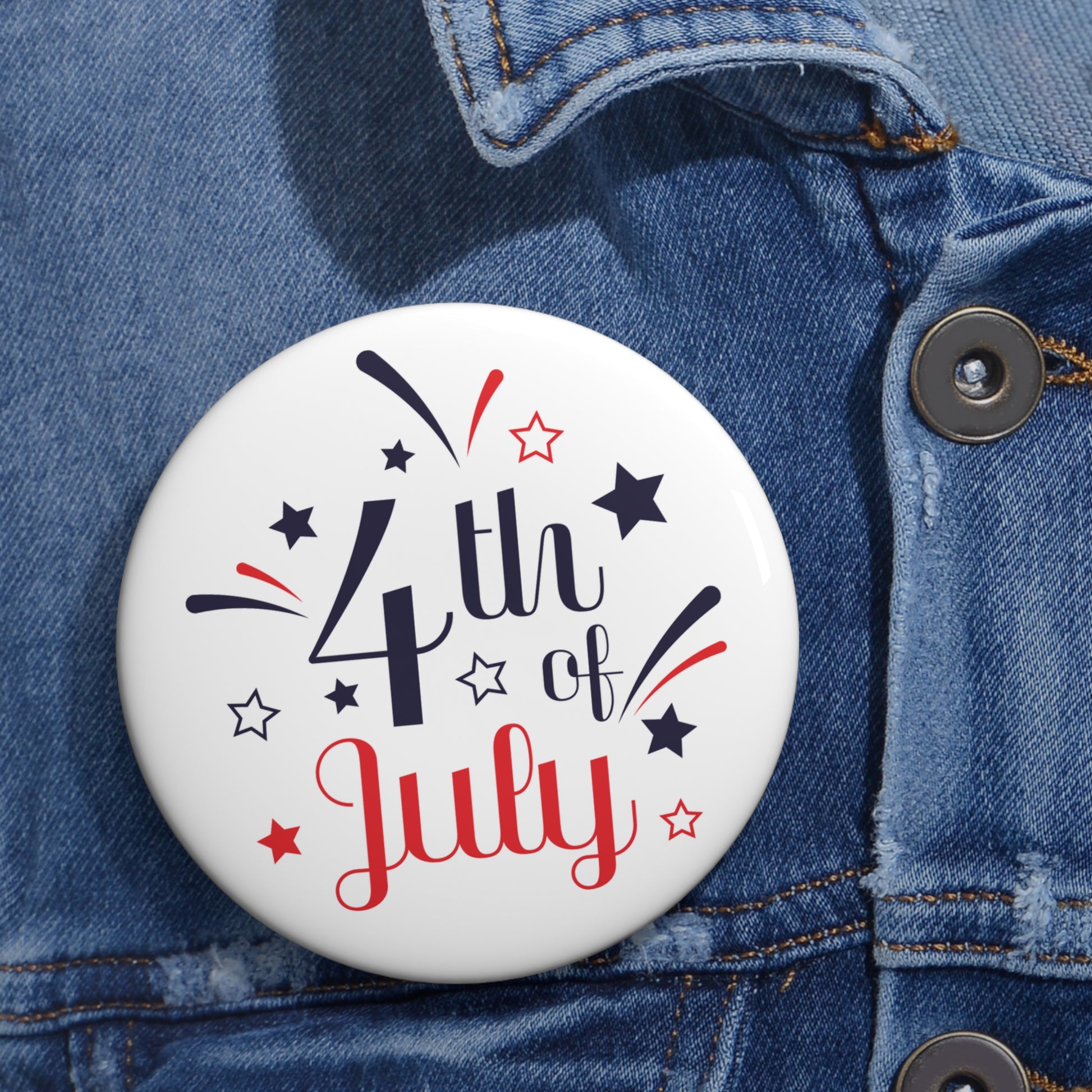 Button on denim jacket with "4th of July" text and star decorations, secured with a safety pin backing. Product: 4th of July Buttons: 2 sizes; Lightweight metal; Graphics by Printify.