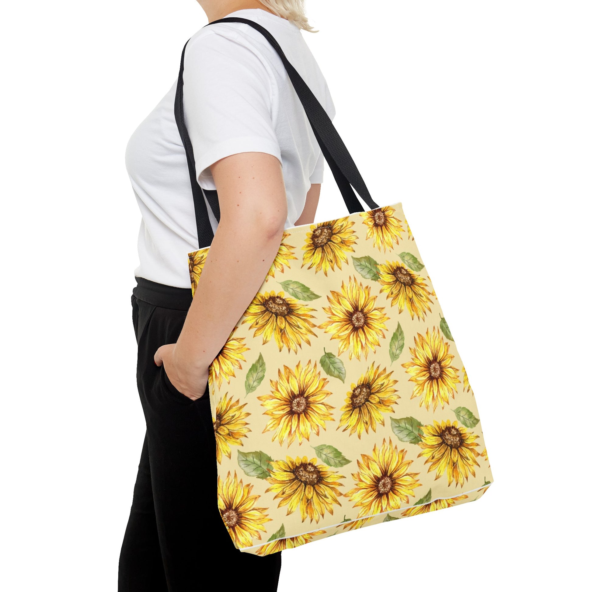 A person wearing a white t-shirt and black pants carries a large Yellow Floral Tote Bag with sunflower print from Printify.