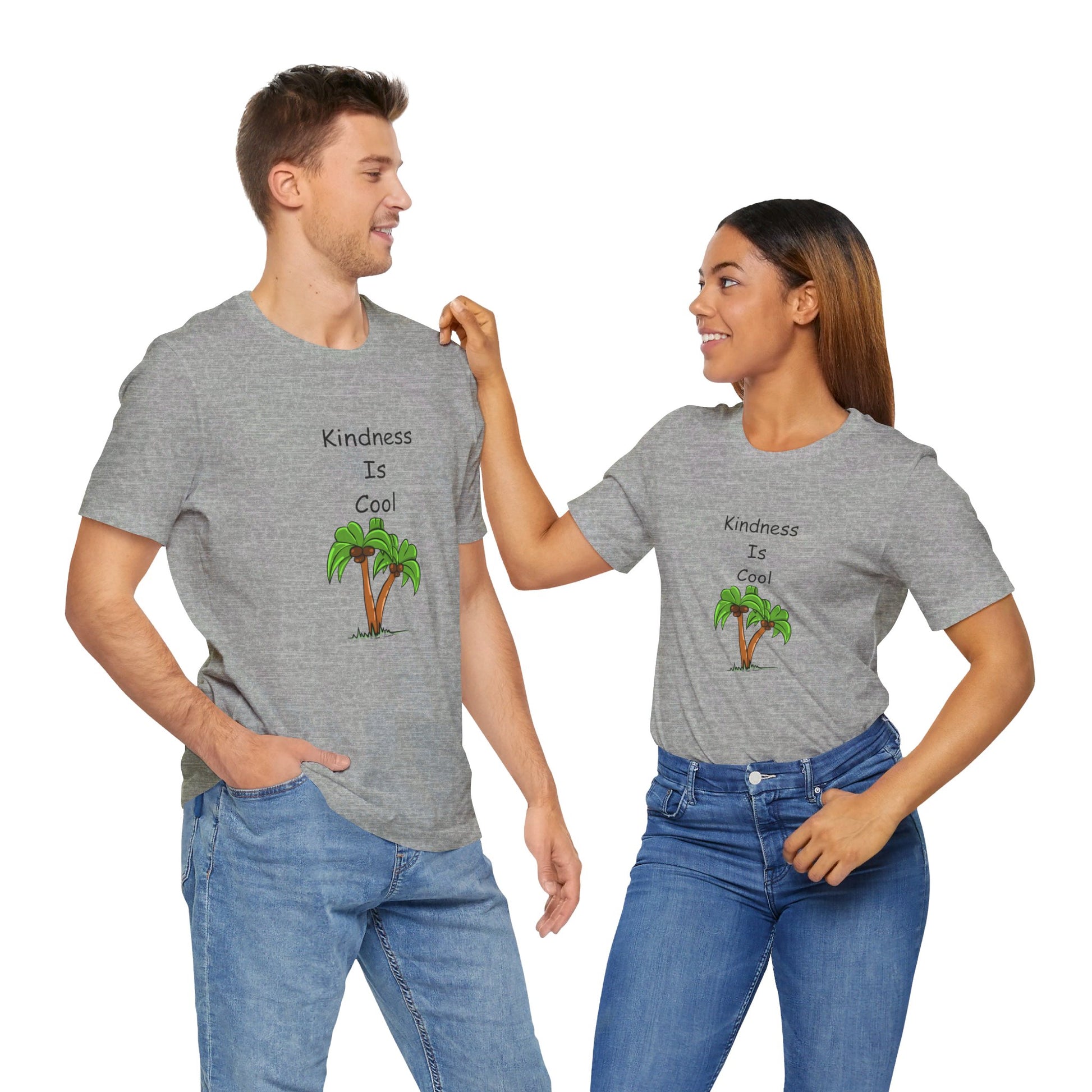 Two people are standing side by side, wearing matching gray Unisex Kindness-Is-Cool T-shirts from Printify, made of soft cotton jersey by Bella+Canvas. The shirts feature the text "Kindness-Is-Cool" and an image of a palm tree. They are smiling at each other.