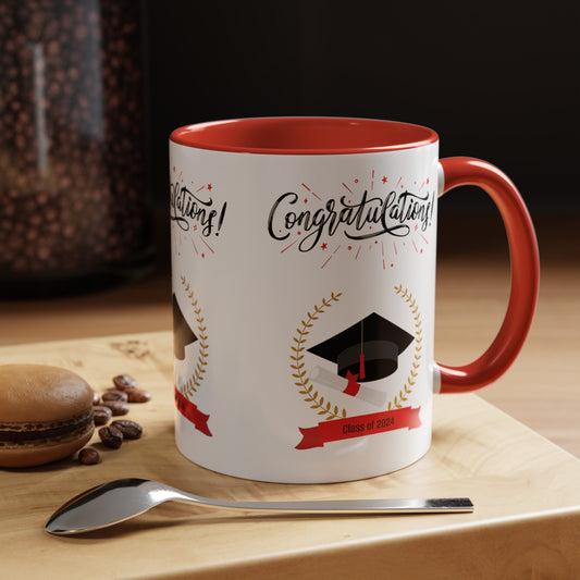 A custom white coffee mug with a red handle and interior sits on a wooden surface, featuring graduation-themed graphics and the text "Congratulations! Class of 2024." A spoon and a macaron are nearby. Celebrate your achievement with this 2024 Graduation Mug: 11 oz.; 2 colors; Ceramic; Accented by Printify, now available with free shipping.