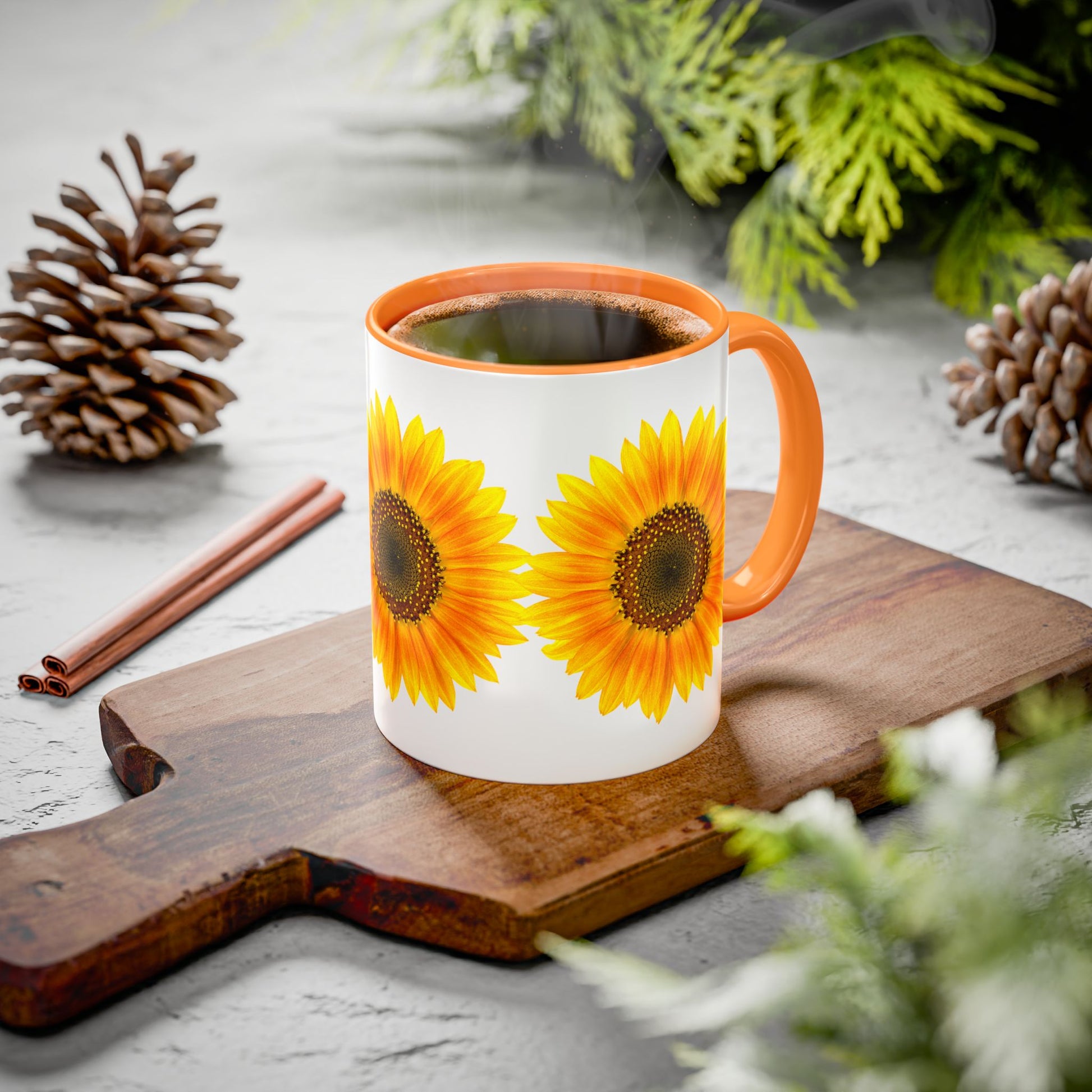 The Sunflower Coffee Mug: Bright Floral | 11oz ceramic cup by Printify, featuring two sunflower prints and orange accents, rests on a wooden board surrounded by pinecones, cinnamon sticks, and greenery.