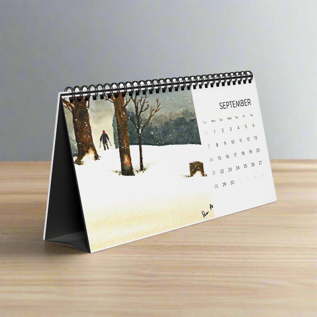 The 2025 Desktop Calendar: Snowshoe Hiker by Printify is open to September, featuring a watercolor painting of a snowy landscape. This captivating artwork beautifully portrays trees and a person walking, making it an ideal selection for nature enthusiasts who wish to experience serenity in their daily routine.