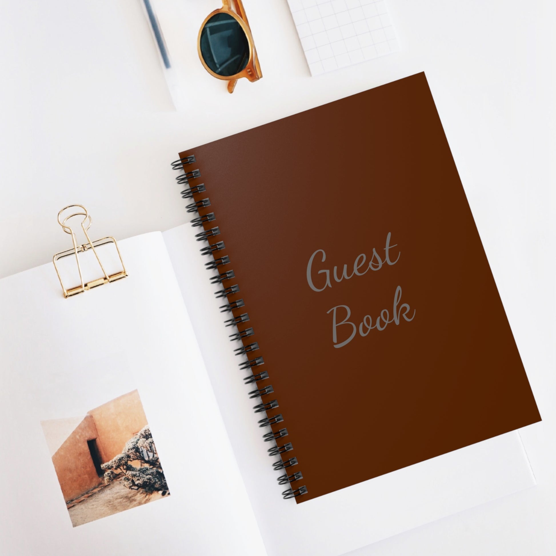 A Printify unisex spiral-bound guest book: 6" x 8"; 118 ruled lines for wedding receptions, placed on a white surface surrounded by office supplies and a photo.