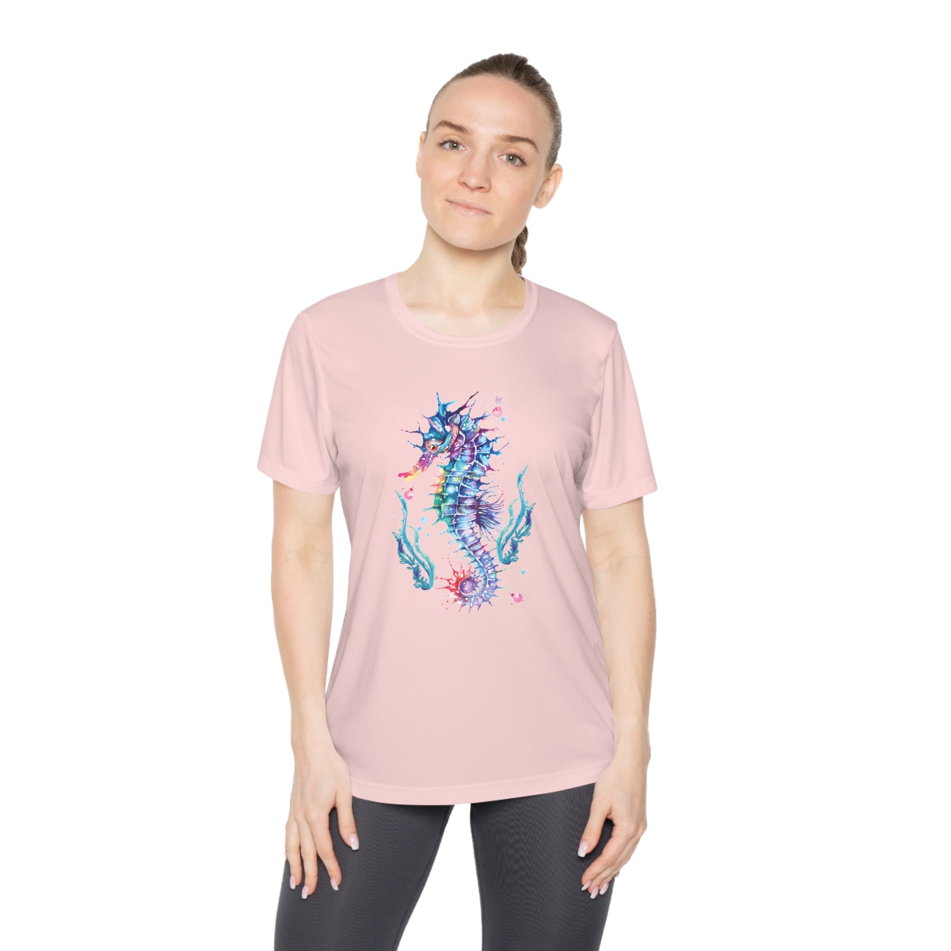 A person wearing a Printify Moisture-wicking Ladies T-shirt: Seashorse; Sport Tek 350, featuring a feminine fit and moisture-wicking properties, stands in front of a plain background.