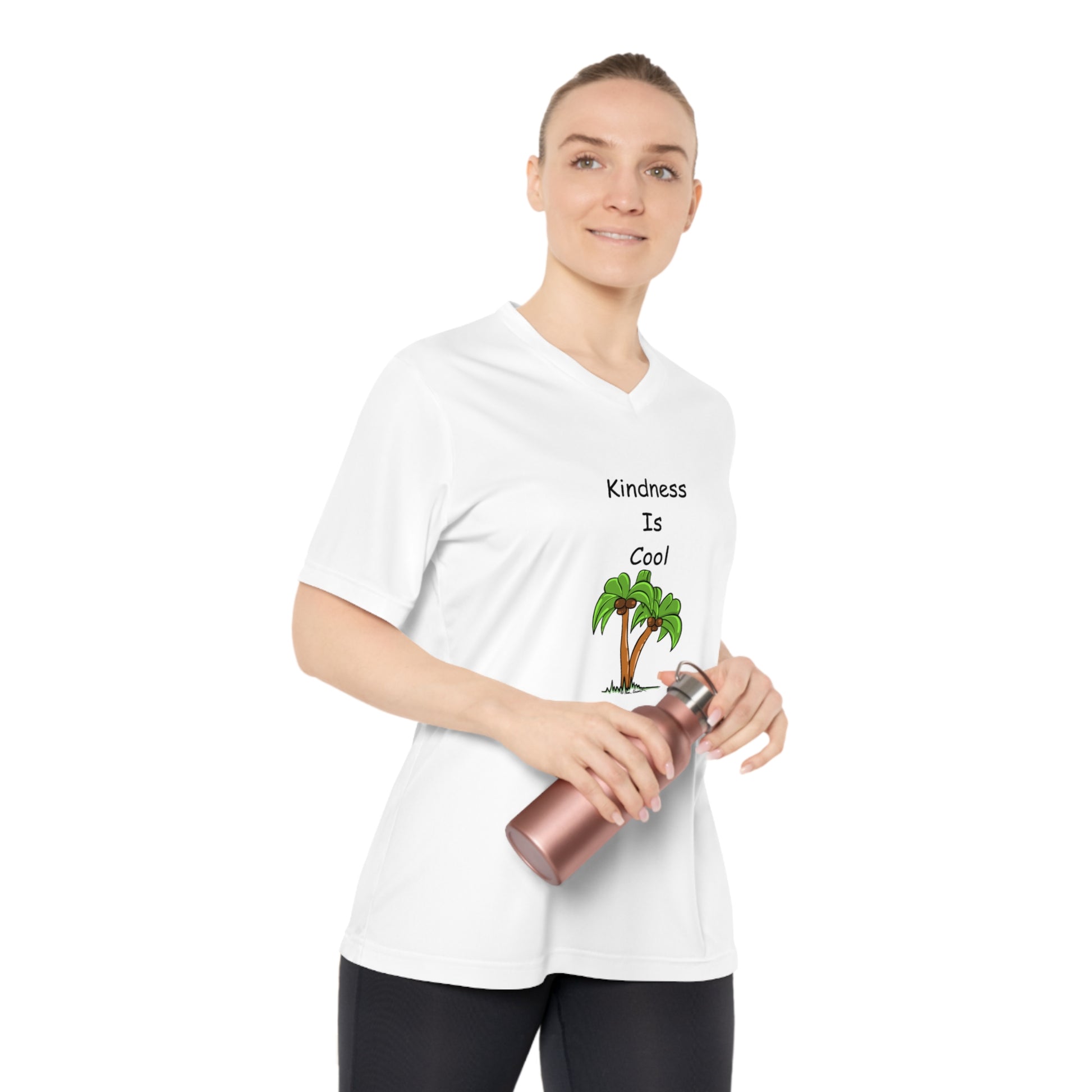 A person wearing a Team 365 Women's Kindness-Is-Cool V-neck T-shirt in moisture-wicking polyester with UV 40+ protection by Printify, featuring "Kindness is Cool" text and a palm tree graphic, holding a metallic water bottle.