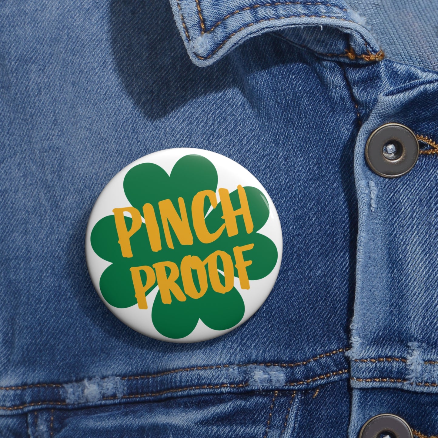 The Printify Metal Pin Button, available in 2 sizes, features a green shamrock and "Pinch Proof" text—an ideal unisex accessory for St. Patrick's Day, shown pinned to a blue denim jacket.