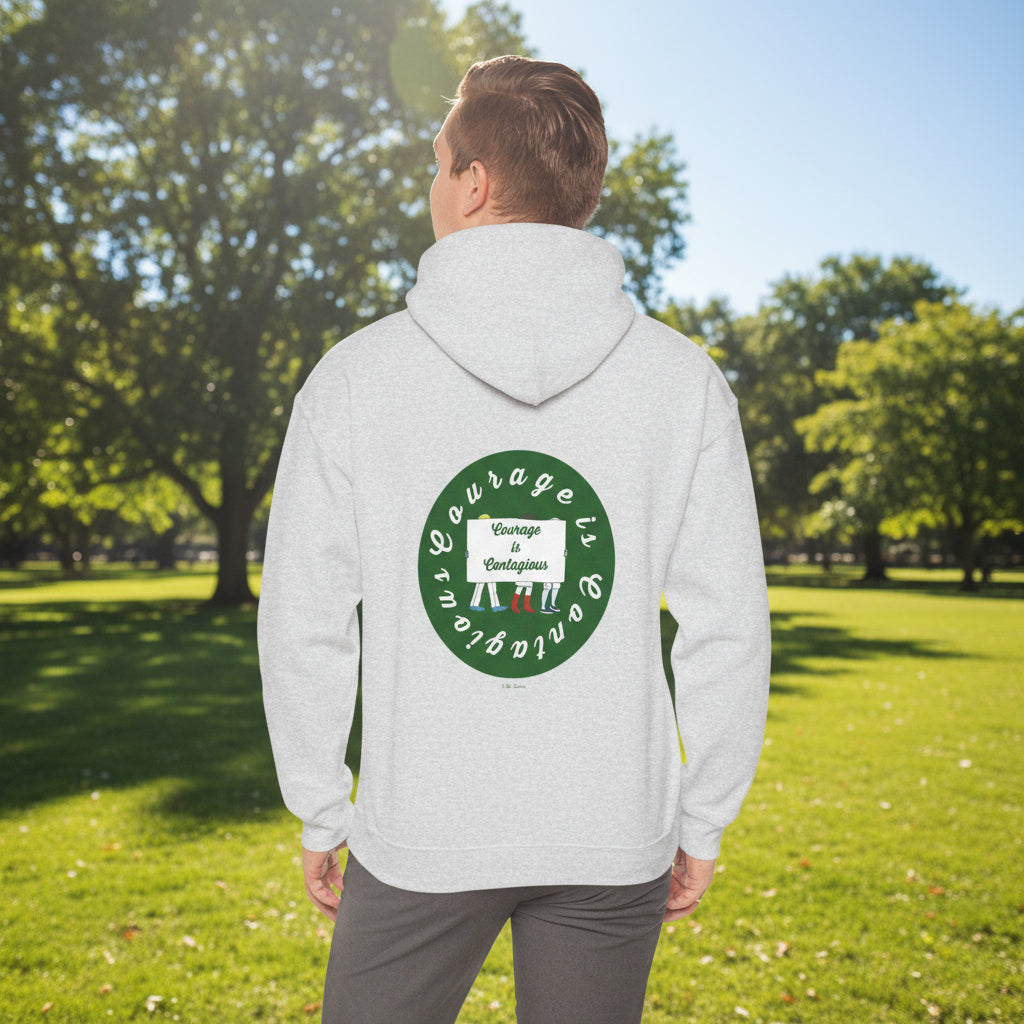 Outdoors, a person wears the Printify Courage Is Contagious Hoodie: Mental Health Awareness—an ethically made, light gray sweatshirt with a circular green emblem and raised fists on the back, spreading a powerful message.